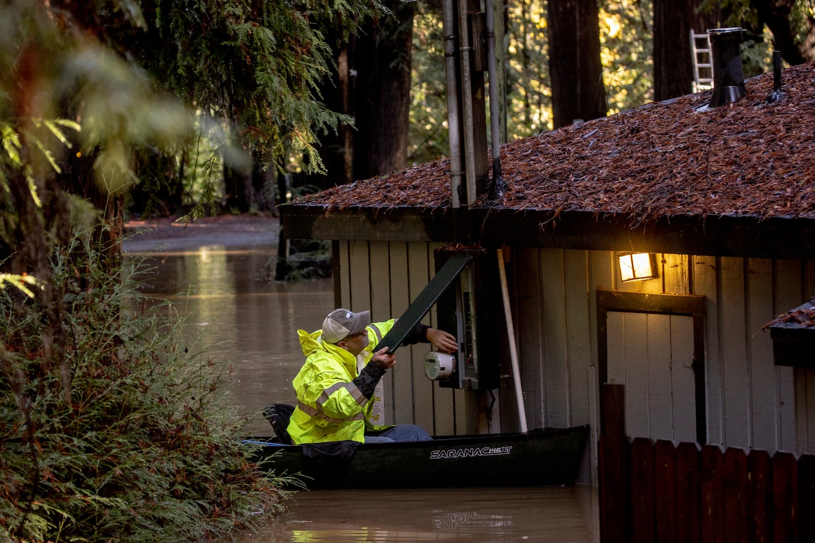 Sitting on a canoe, John Phillips works to shut down power at a flooded building at Mirabel RV Park & Campground after a major storm in Forestville, Calif., Saturday, Nov. 23, 2024. (Stephen Lam/San Francisco Chronicle via AP)