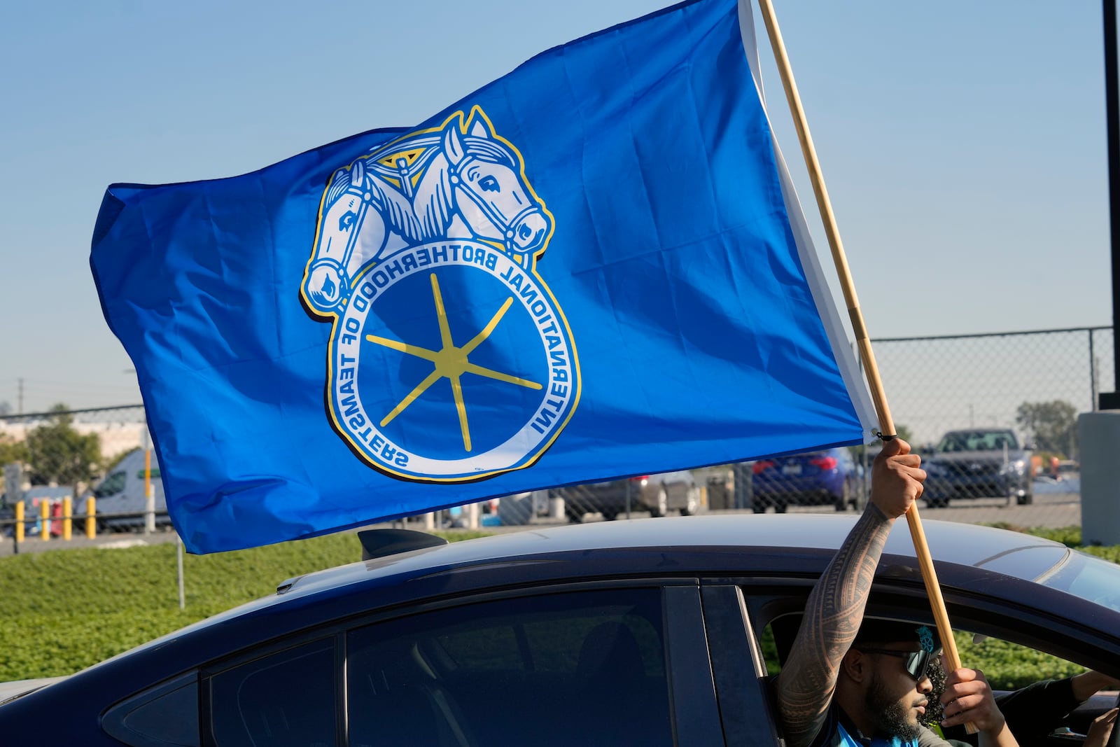 A supporter waving a Teamster flag rides past Amazon workers striking outside the gates of an Amazon Fulfillment Center on Friday, Dec. 20, 2024, in City of Industry, Calif. (AP Photo/Damian Dovarganes)