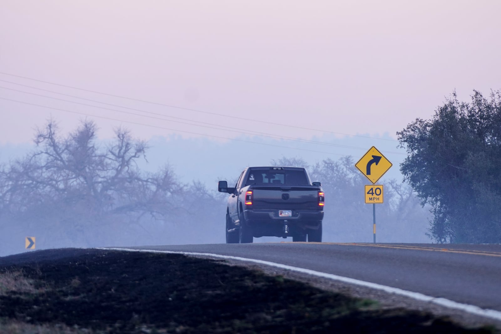 Smoke from the Crabapple Fire drifts over Ranch Road 1631 early Sunday morning, March 16, 2025, in Fredricksburg, Texas. (Robin Jerstad/The San Antonio Express-News via AP)