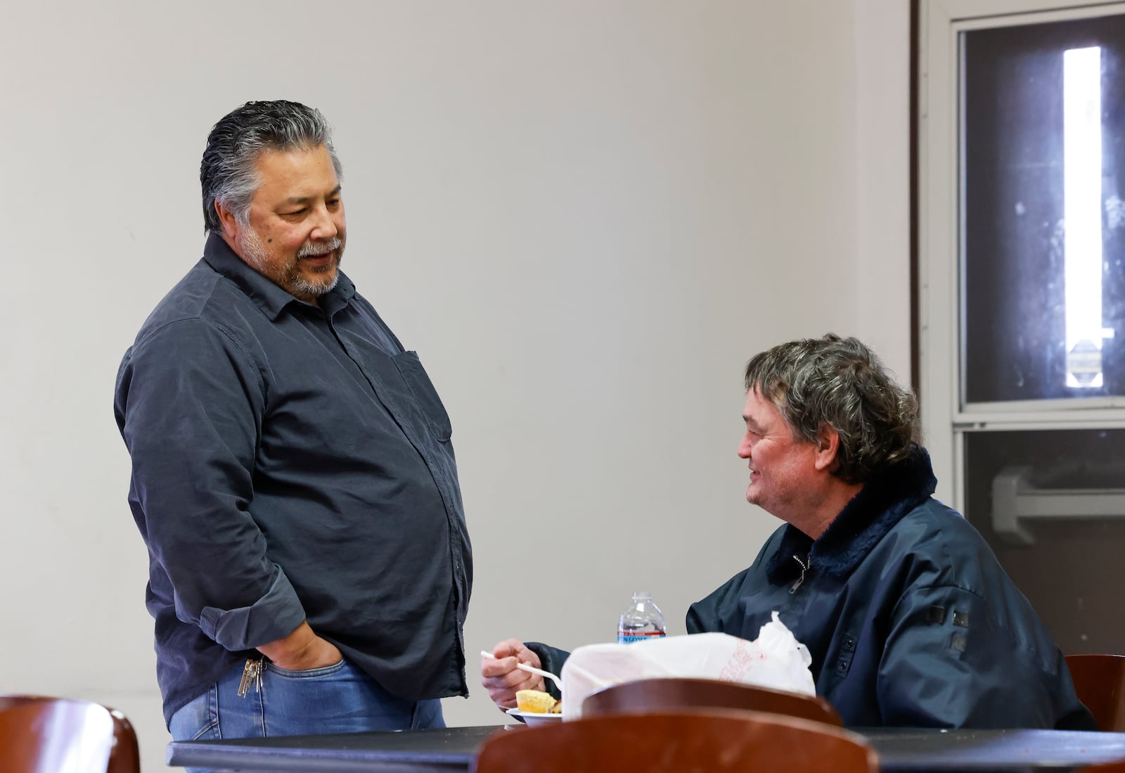 Felix Russo, left, pastor and director of New Life Mission on Henry Street in Hamilton, talks to Mark Cole as he eats lunch at the at the food pantry Thursday, Jan. 4, 2024. Russo said they have seen an increase in clients since the temporary closure of Serve City's food pantry. NICK GRAHAM/STAFF