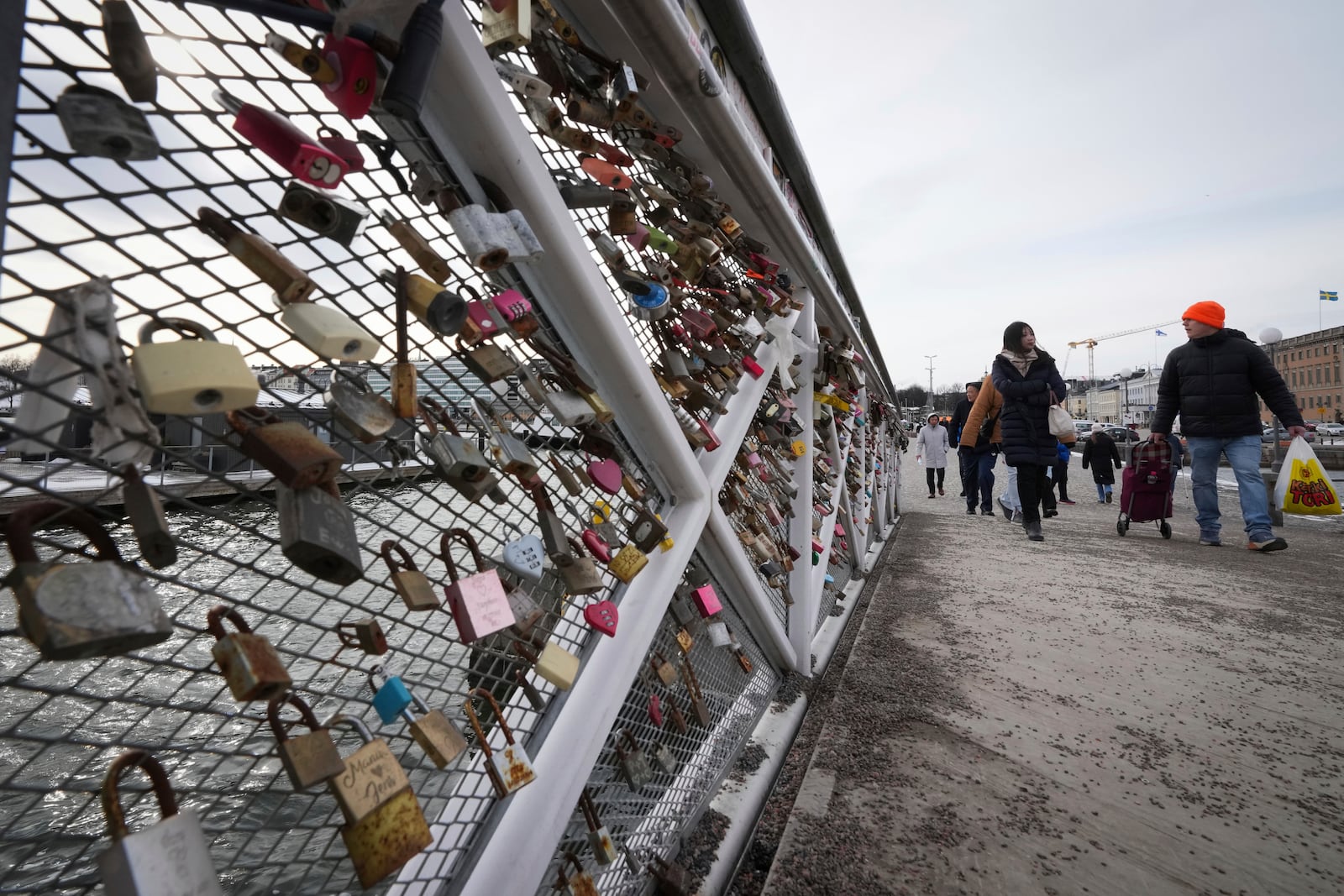 People walk over the iron footbridge decorated with love locks on the Market Square in the center of Helsinki, Finland, Saturday, March 15, 2025. (AP Photo/Sergei Grits)