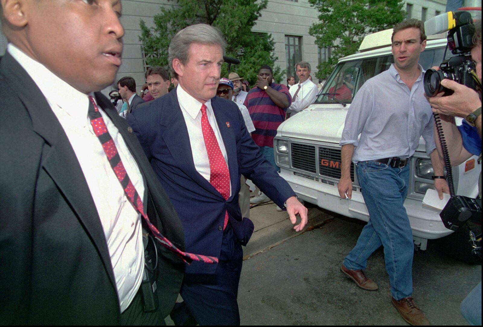 FILE - Arkansas Gov. Jim Guy Tucker, center, leaves the federal courthouse with a security guard in Little Rock, Ark., May 28, 1996. (AP Photo/Danny Johnston, File)