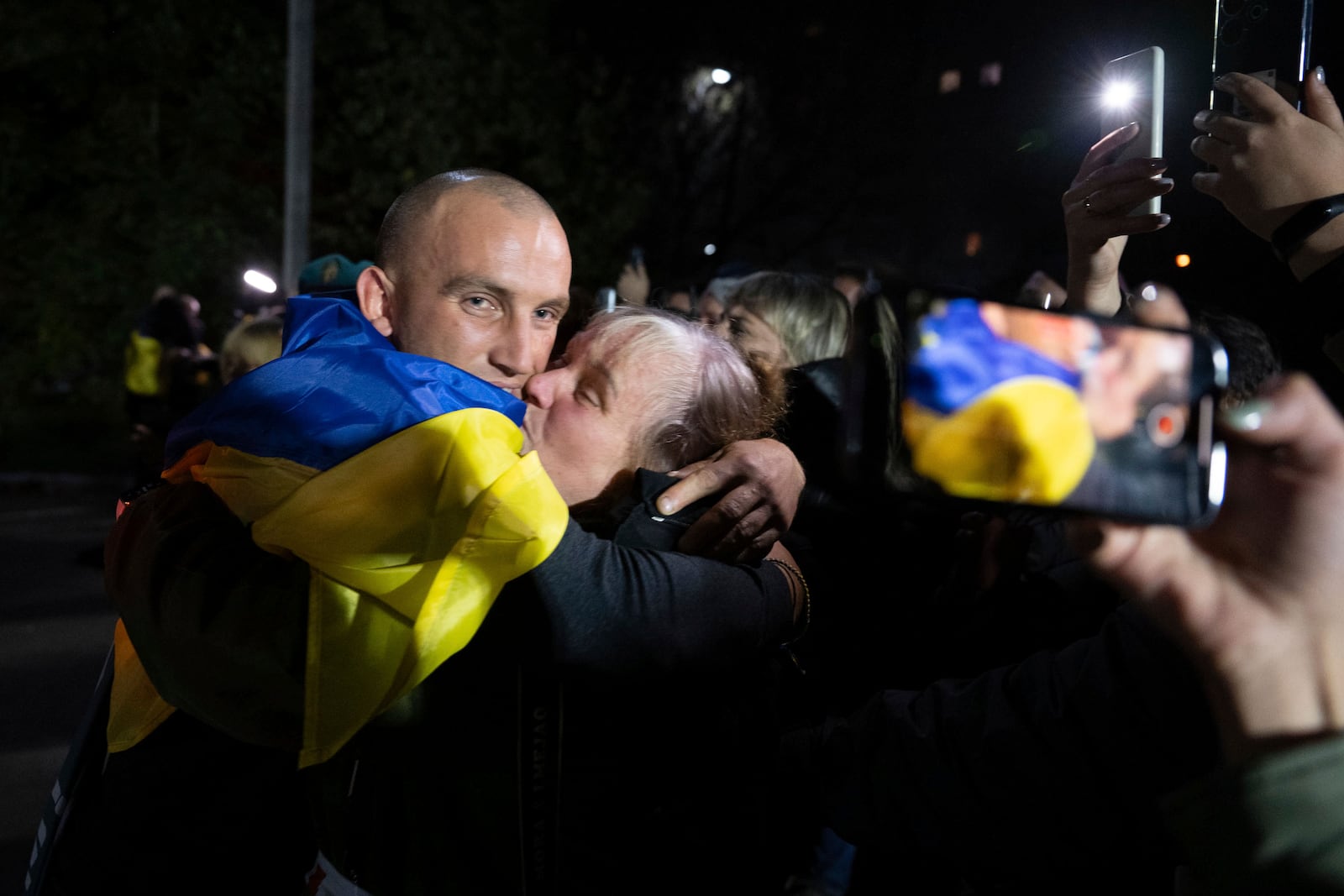 In this photo provided by the Press Service of the President of Ukraine on Oct. 19, 2024, a Ukrainian serviceman with National flag hugs his relative after returning from captivity during a POWs exchange in an undisclosed location, Ukraine. (Press Service of the President of Ukraine via AP)