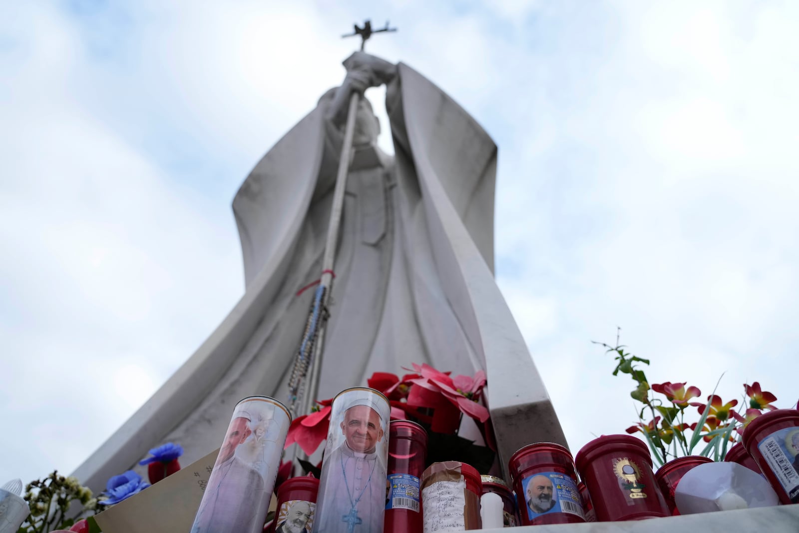 Candles with the pictures of Pope Francis are the laid under the statue of late Pope John Paul II outside Agostino Gemelli Polyclinic in Rome, Wednesday, Feb. 19, 2025, where the Pontiff is hospitalized since Friday, Feb. 14. (AP Photo/Gregorio Borgia)