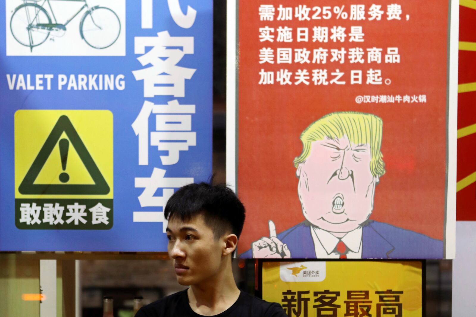 FILE - A man sits in front of a billboard stating that American customers will be charged 25% extra due to ongoing China-U.S. trade tensions at a restaurant in Guangzhou in southern China's Guangdong Province on Aug. 13, 2018. (Chinatopix via AP, File)