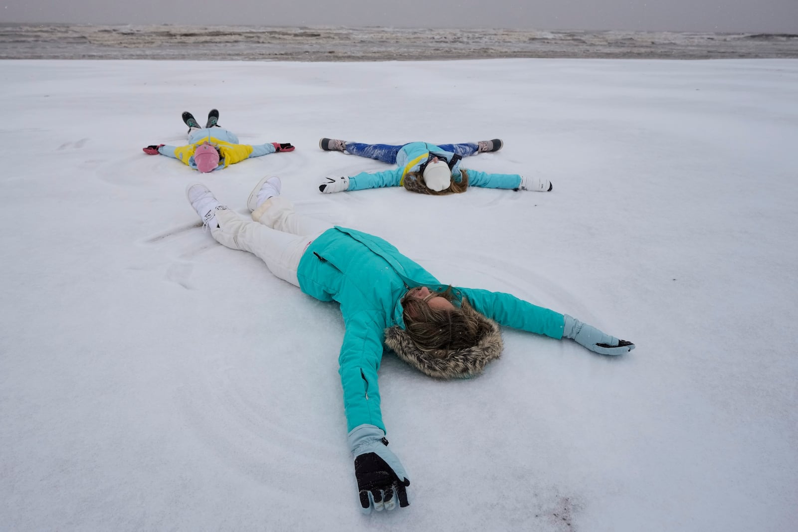 Madison Gaido, and her sisters, Ellie and Kate make snow angels on the beach during an icy winter storm on Tuesday, Jan. 21, 2025 in Galveston, Texas. (Brett Coomer/Houston Chronicle via AP)