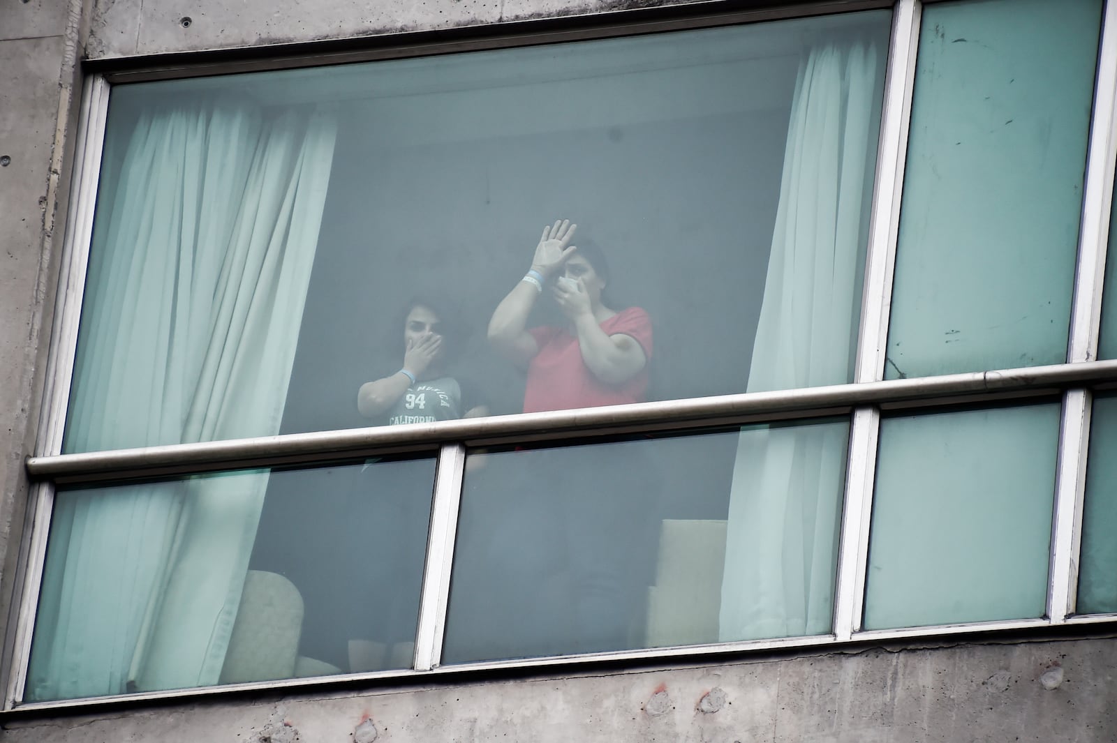 Migrants deported from the United States wave to the press from inside a hotel in Panama City, Wednesday, Feb. 19, 2025. (AP Photo/Agustin Herrera)