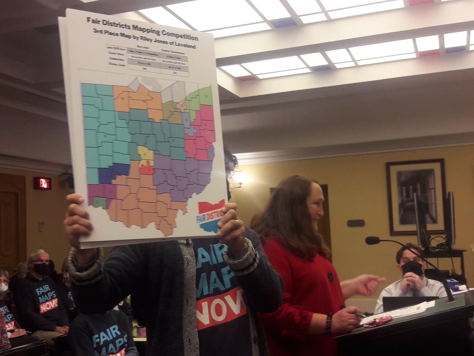 Catherine Turcer, executive director of Common Cause Ohio, speaks to the Ohio Redistricting Commission as Trevor Martin holds up a map proposal for new Ohio congressional districts on Oct. 28, 2021.