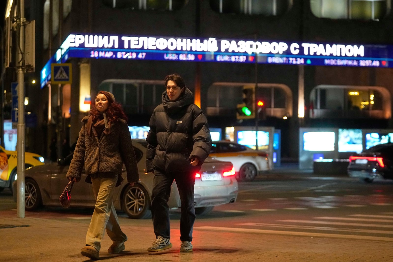 People cross a street with a news ticker in the background reporting on a phone call between Russian President Vladimir Putin and US President Donald Trump, on the facade of TASS news agency building in Moscow, Russia, Tuesday, March 18, 2025. (AP Photo/Pavel Bednyakov)