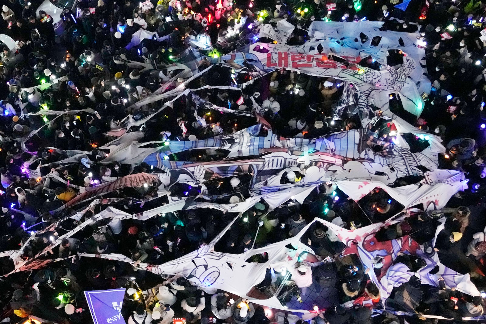 Participants tear a banner depicting South Korean President Yoon Suk Yeol's face on a cartoon train during a rally to demand his impeachment in front of the headquarters of the ruling People Power Party in Seoul, South Korea, Friday, Dec. 13, 2024. (AP Photo/Ahnn Young-joon)