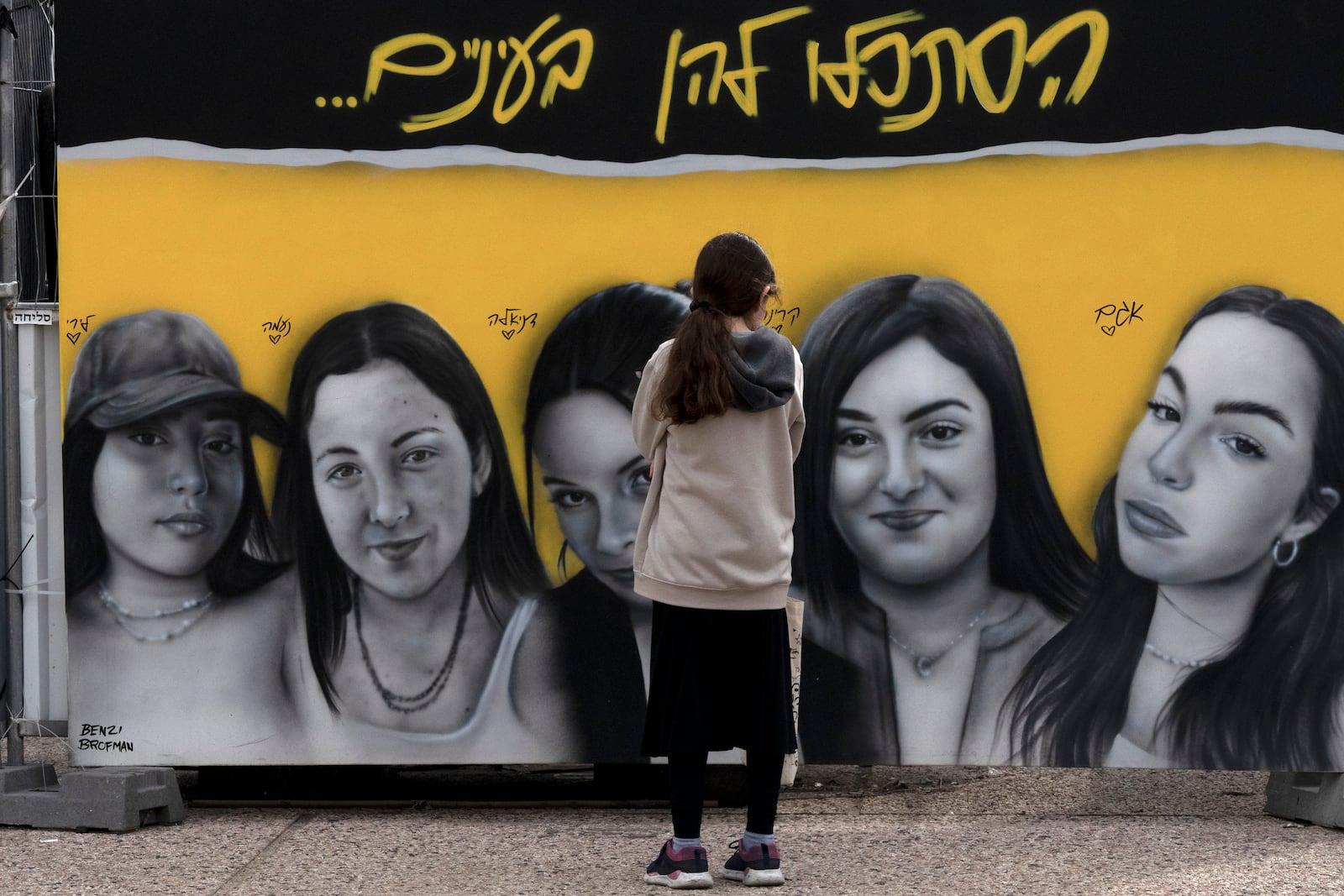 A girl pauses at a mural of female Israeli soldiers held by Hamas in the Gaza Strip, in Tel Aviv, Israel, as Israel's security cabinet convened to decide whether to approve a deal that would release dozens of hostages held by militants in Gaza and pause the 15-month-war, Friday, Jan. 17, 2025. Hebrew reads: "look them in the eyes." (AP Photo/Maya Alleruzzo)