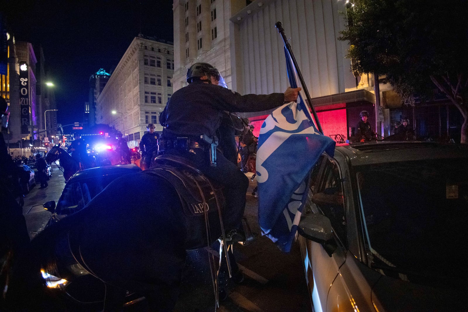 A police officer on horseback grabs a Los Angeles Dodgers flag as people gather on the streets after the Los Angeles Dodgers won against the New York Yankees in the baseball World Series Wednesday, Oct. 30, 2024, in Los Angeles. (AP Photo/Ethan Swope)