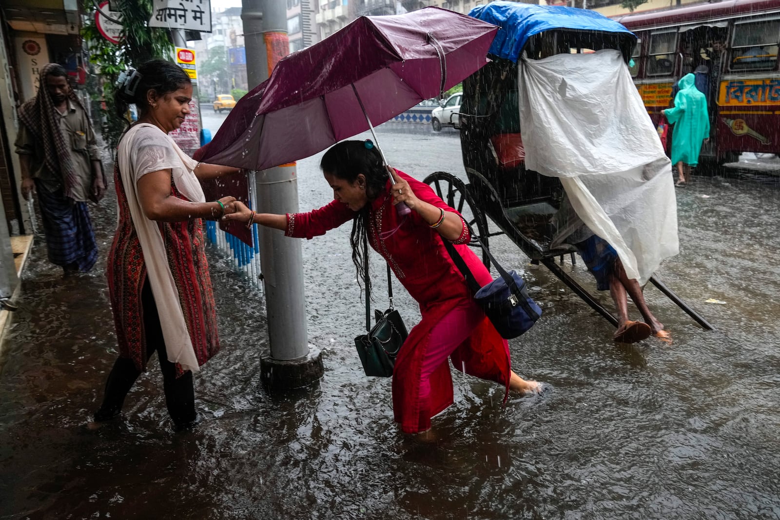 A woman helps another to wade through a waterlogged road during heavy rain following tropical storm Dana, in Kolkata, India, Friday, Oct. 25, 2024. (AP Photo/Bikas Das)