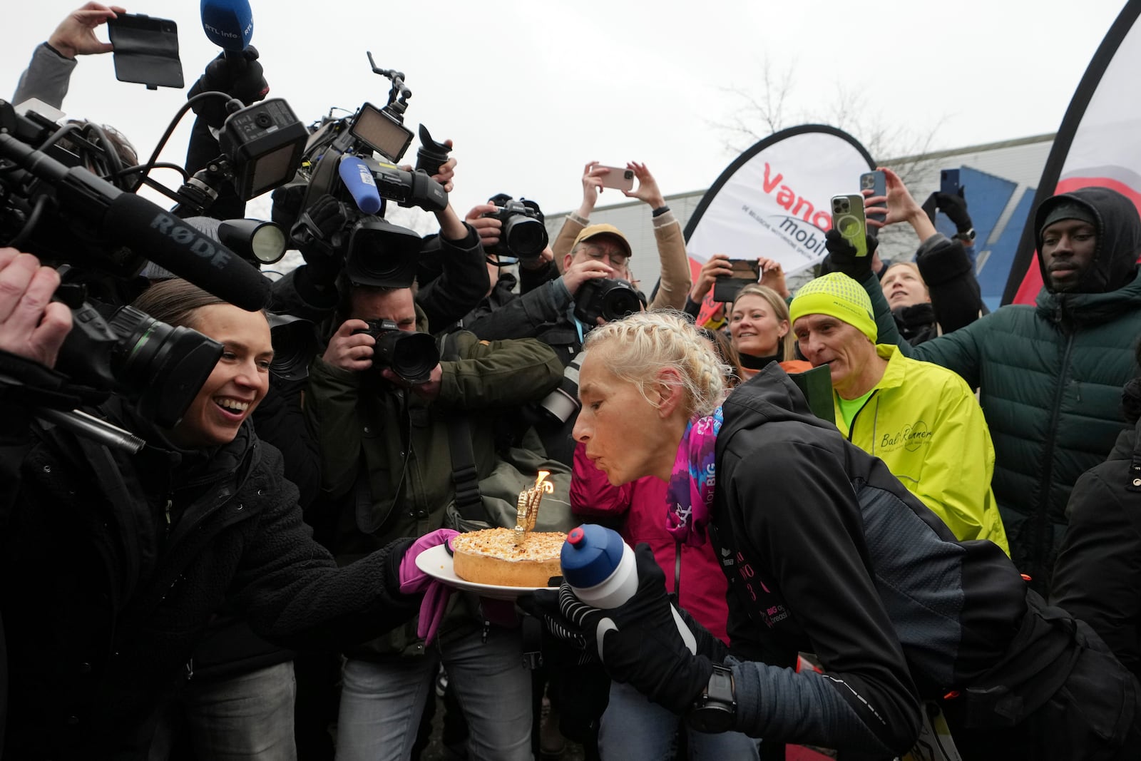 Belgian ultra runner Hilde Dosogne, center, blows out candles on a cake after crossing the finish line of her 366th consecutive marathon in Ghent, Belgium, Tuesday, Dec. 31, 2024. (AP Photo/Virginia Mayo)