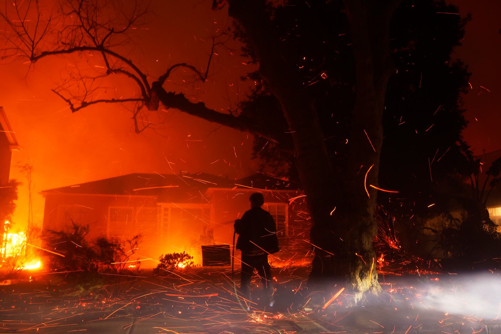 FILE - A person tries to hose down embers from the Palisades Fire in the Pacific Palisades neighborhood of Los Angeles, Jan. 7, 2025. (AP Photo/Etienne Laurent, File)