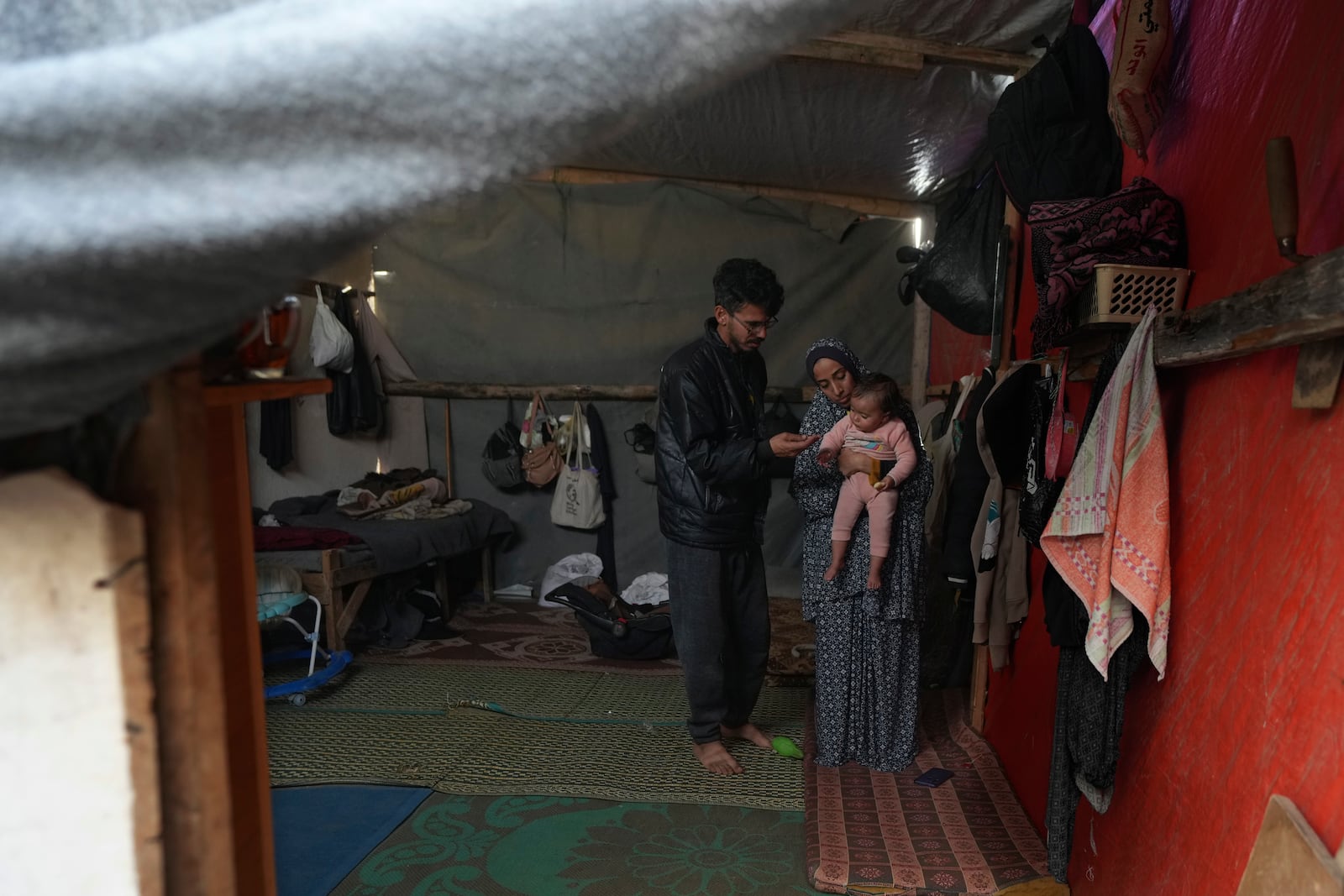 Rola Saqer and her husband Mohammad Zaqout, center, stand with their daughter, Massa Zaqout, who was born on the first day of the war in Gaza, in the family tent in Deir al-Balah, Gaza Strip, Tuesday, Jan. 14, 2025. (AP Photo/Abdel Kareem Hana)