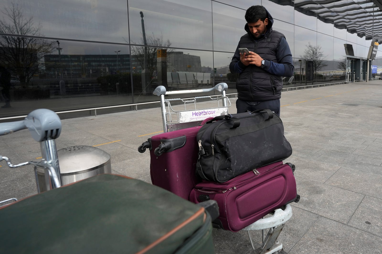 Omar Sheikh from Pakistan checks his phone whilst standing beside his lugage at Terminal 4 as Britain's Heathrow Airport has closed for the full day Friday after an electrical substation fire knocked out its power, disrupting flights for hundreds of thousands of passengers at one of Europe's biggest travel hubs in London, Friday, March 21, 2025.(AP Photo/Kin Cheung)