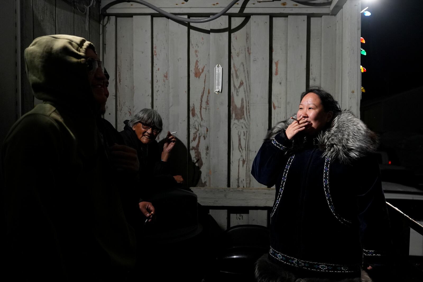 Kitty Ahvakana, right, takes a smoke break with other villagers during a "singspiration" gathering on the porch of the community center in Kaktovik, Alaska, Monday, Oct. 14, 2024. (AP Photo/Lindsey Wasson)