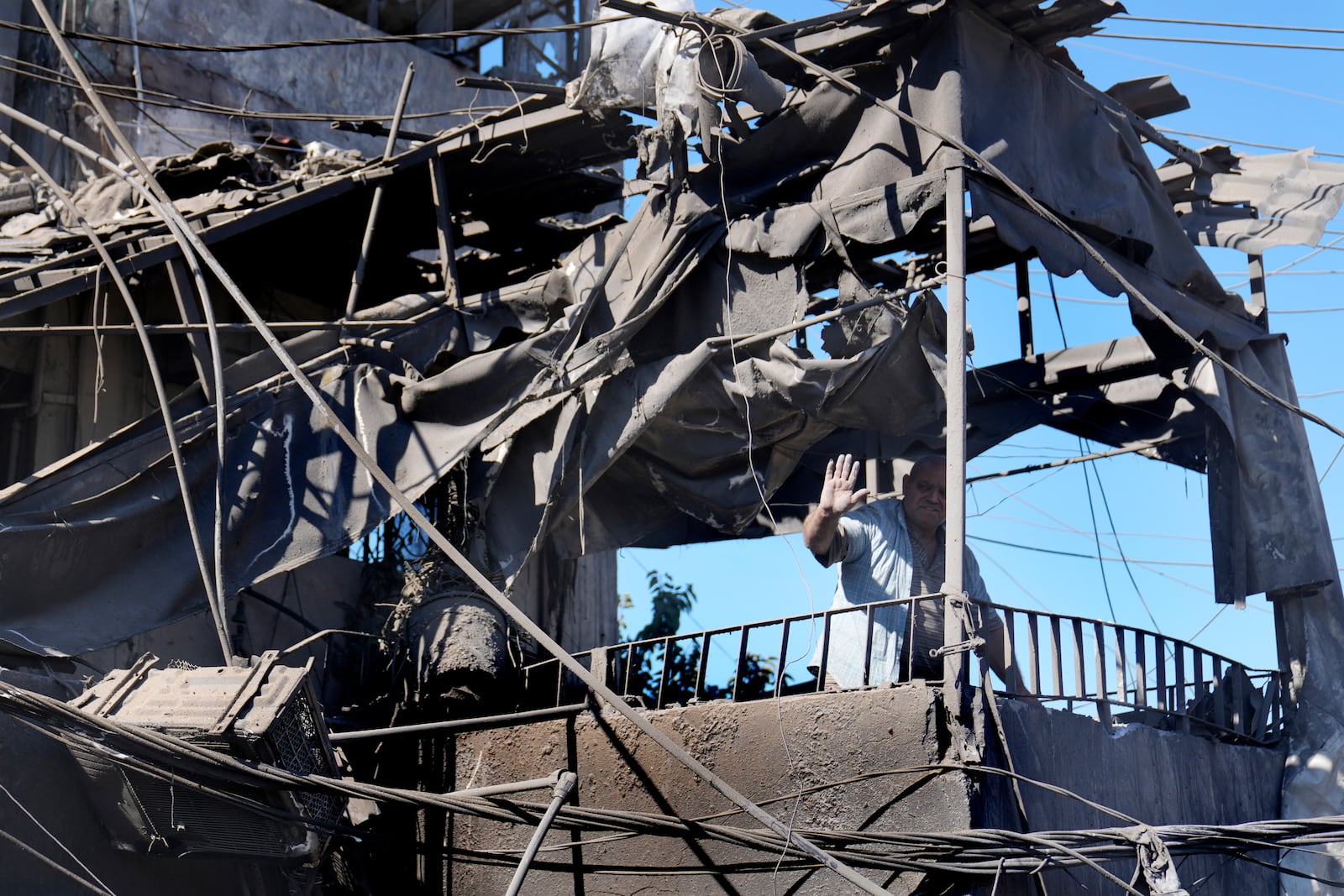 A man waves from his shattered house at the site of Israeli airstrikes that destroyed buildings facing the city's main government hospital in a densely-populated neighborhood, in southern Beirut, Lebanon, Tuesday, Oct. 22, 2024. (AP Photo/Hussein Malla)