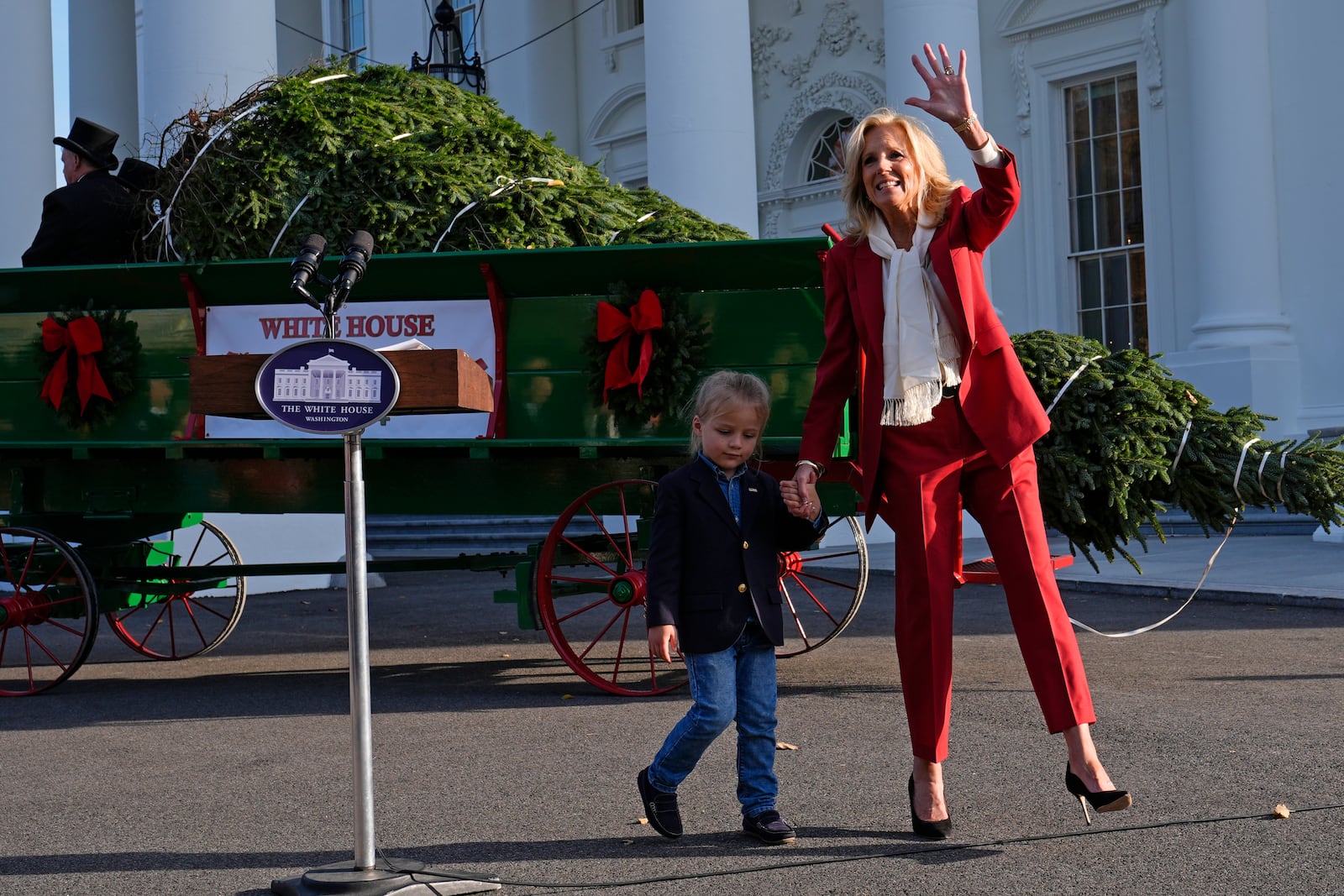 First lady Jill Biden waves as she walks with her grandson Beau Biden after receiving the official 2024 White House Christmas Tree on the North Portico of the White House in Washington, Monday, Nov. 25, 2024. Cartner's Christmas Tree Farm from Newland, N.C., provided the Fraser fir that will be displayed in the Blue Room of the White House. (AP Photo/Susan Walsh)