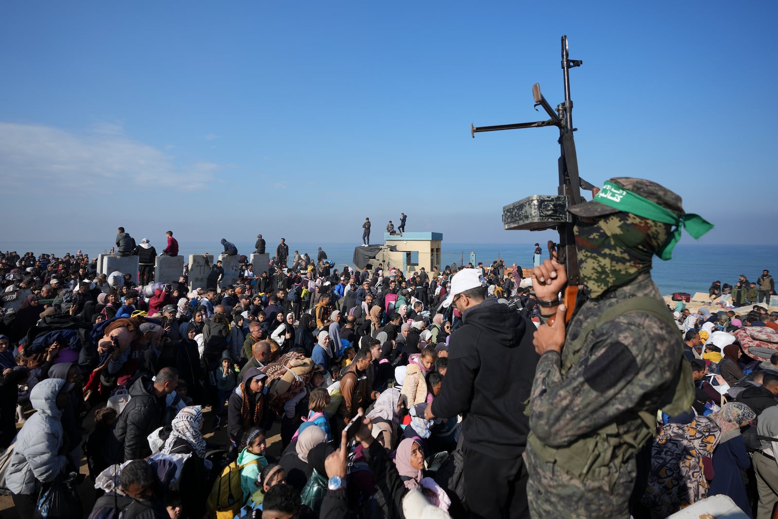 A Hamas fighter lifts his weapon as displaced Palestinians return to their homes in the northern Gaza Strip, Monday, Jan. 27, 2025, following Israel's decision to allow thousands of them to go back for the first time since the early weeks of the 15-month war with Hamas. (AP Photo/Abdel Kareem Hana)