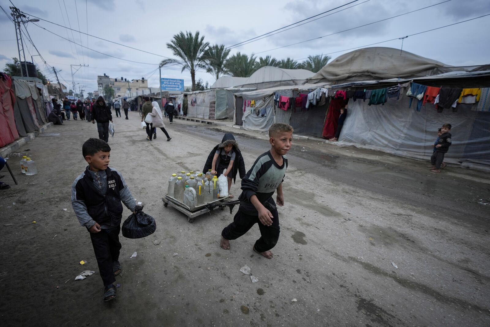 Palestinian children push a cart carrying jerrycans and plastic bottles of water at a camp for displaced people in Deir al-Balah, Gaza Strip, on Thursday, Dec. 12, 2024. (AP Photo/Abdel Kareem Hana)