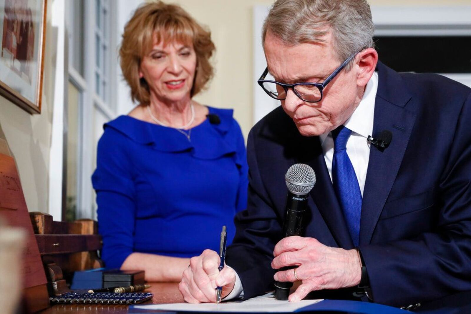 Ohio Gov. Mike DeWine signs one of six executive actions alongside his wife Fran, left, Monday, Jan. 14, 2019, in Cedarville, Ohio. The former U.S. senator took his oath in a private midnight ceremony at his Cedarville home ahead of a public inauguration planned Monday at the Statehouse.