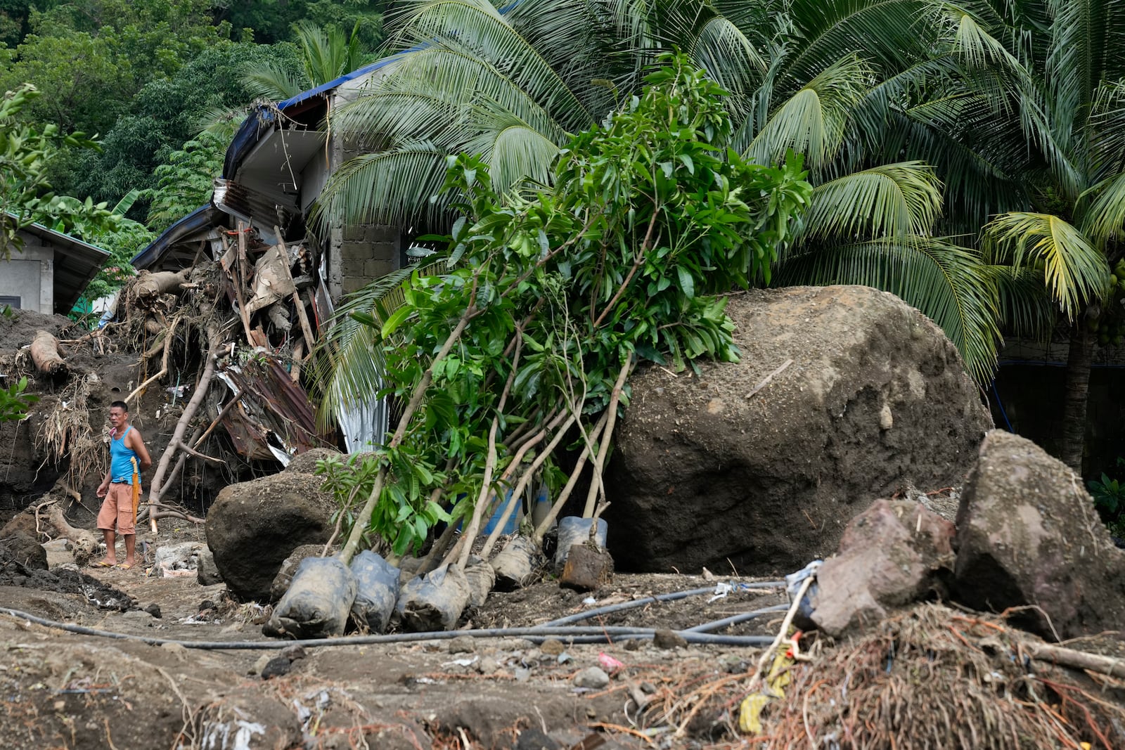 A resident passes by large boulders beside damaged homes on Saturday, Oct. 26, 2024 after being struck by a landslide triggered by Tropical Storm Trami in Talisay, Batangas province, Philippines. (AP Photo/Aaron Favila)