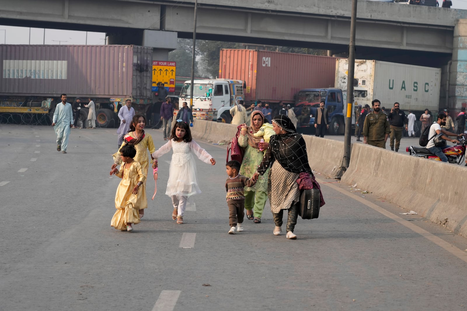 Travellers walk to cross an area barricaded by authorities ahead of a planned rally by supporters of imprisoned former premier Imran Khan's Pakistan Tehreek-e-Insaf party, in Lahore, Pakistan, Sunday, Nov. 24, 2024. (AP Photo/K.M. Chaudary)