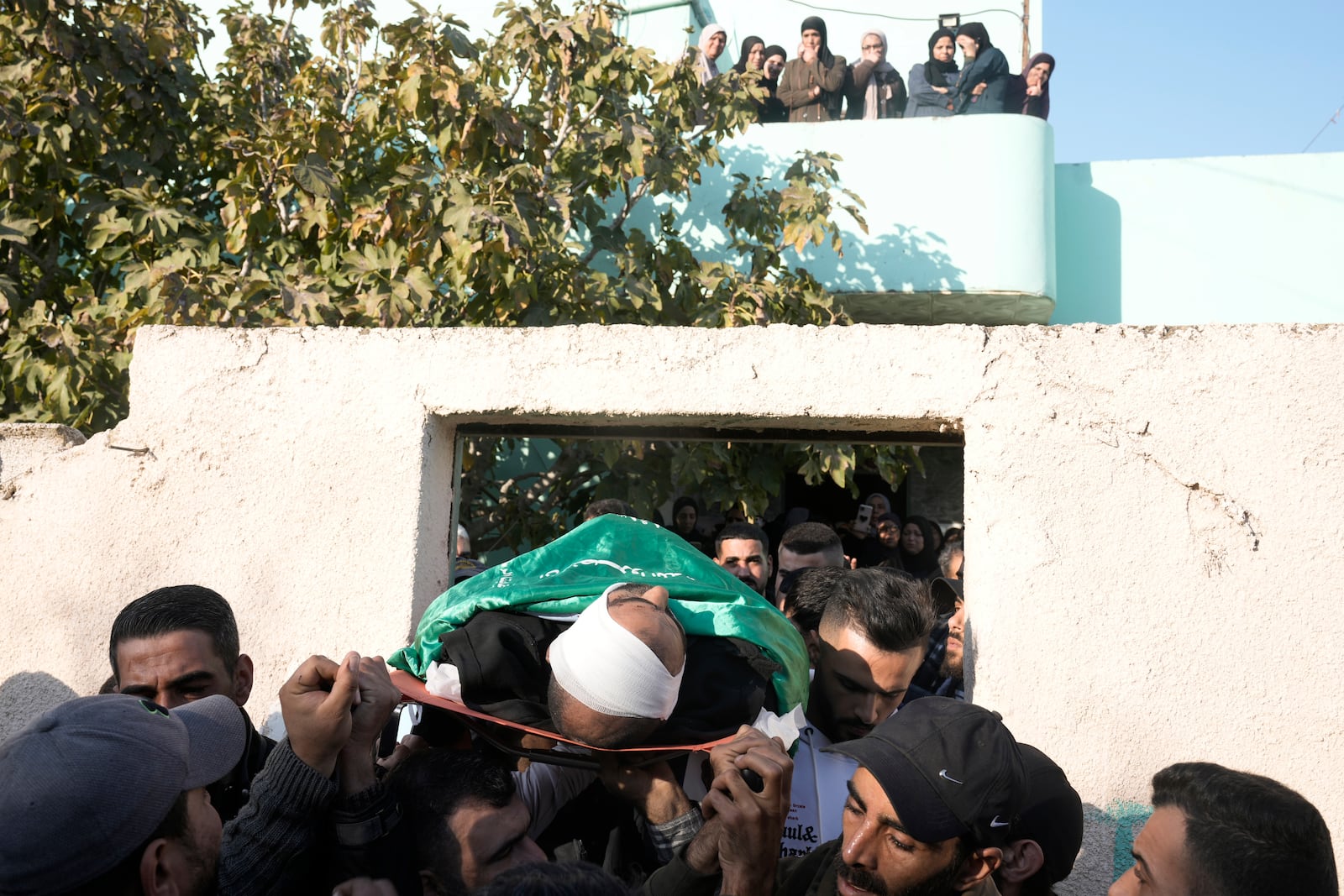 Mourners carry the body of Akram Abu Arrah, wrapped with a Hamas flag, out of the family house during his funeral with Mohammad Ghannam, both killed in an airstrike Israel said targeted a militant cell, in the West Bank village of Al-Aqaba, Tuesday Dec. 3, 2024. (AP Photo/Majdi Muhammad)