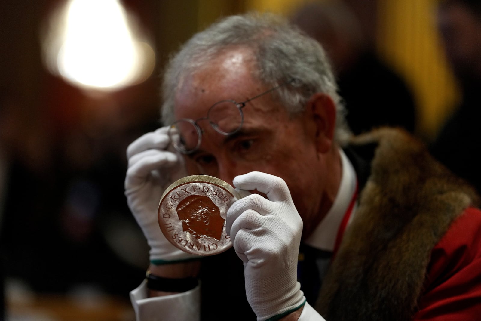 A warden inspects a 500 Pound coin during the "Trial of the Pyx,'' a ceremony that dates to the 12th Century in which coins are weighed in order to make certain they are up to standard, at the Goldsmiths' Hall in London, Tuesday, Feb. 11, 2025.(AP Photo/Frank Augstein)