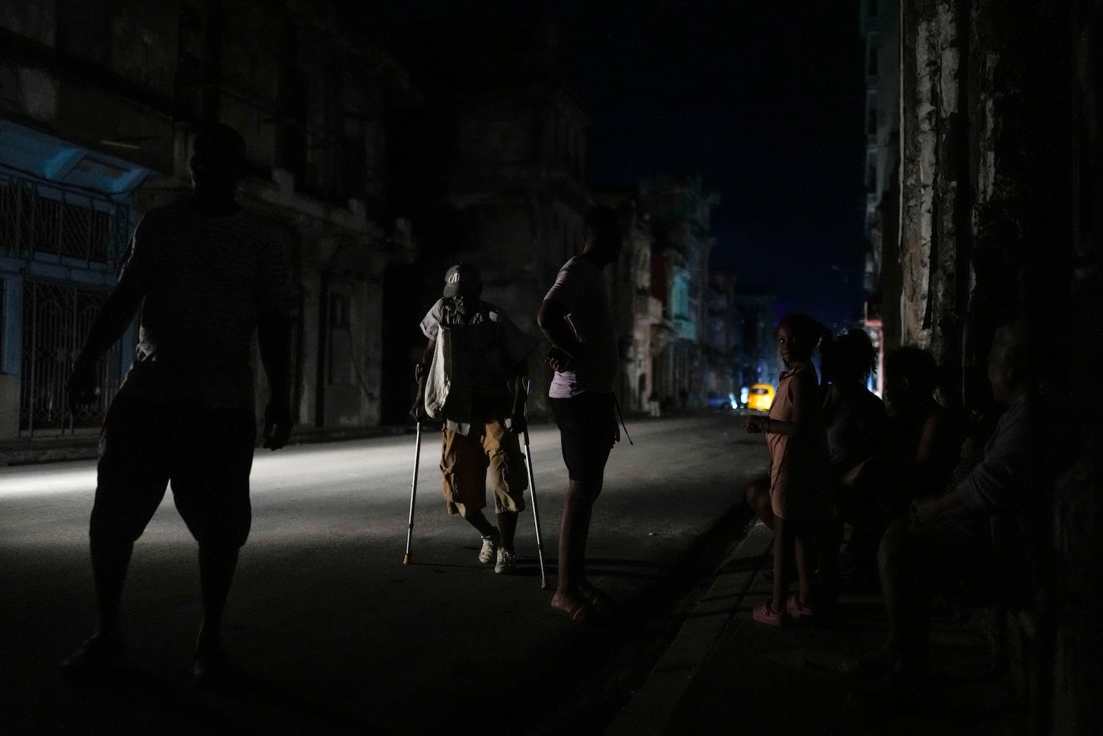 A man walks along a street with the aid of crutches during a massive blackout after a major power plant failed in Havana, Cuba, Friday, Oct. 18, 2024. (AP Photo/Ramon Espinosa)