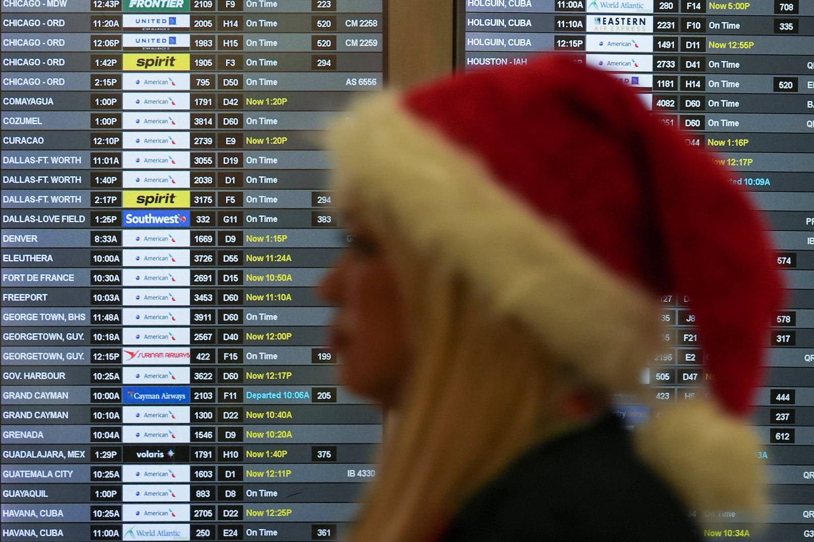 An employee wearing a Santa Claus hat walks past boards showing flight delays, in the American Airlines terminal at Miami International Airport, on Christmas Eve, Tuesday, Dec. 24, 2024, in Miami. (AP Photo/Rebecca Blackwell)