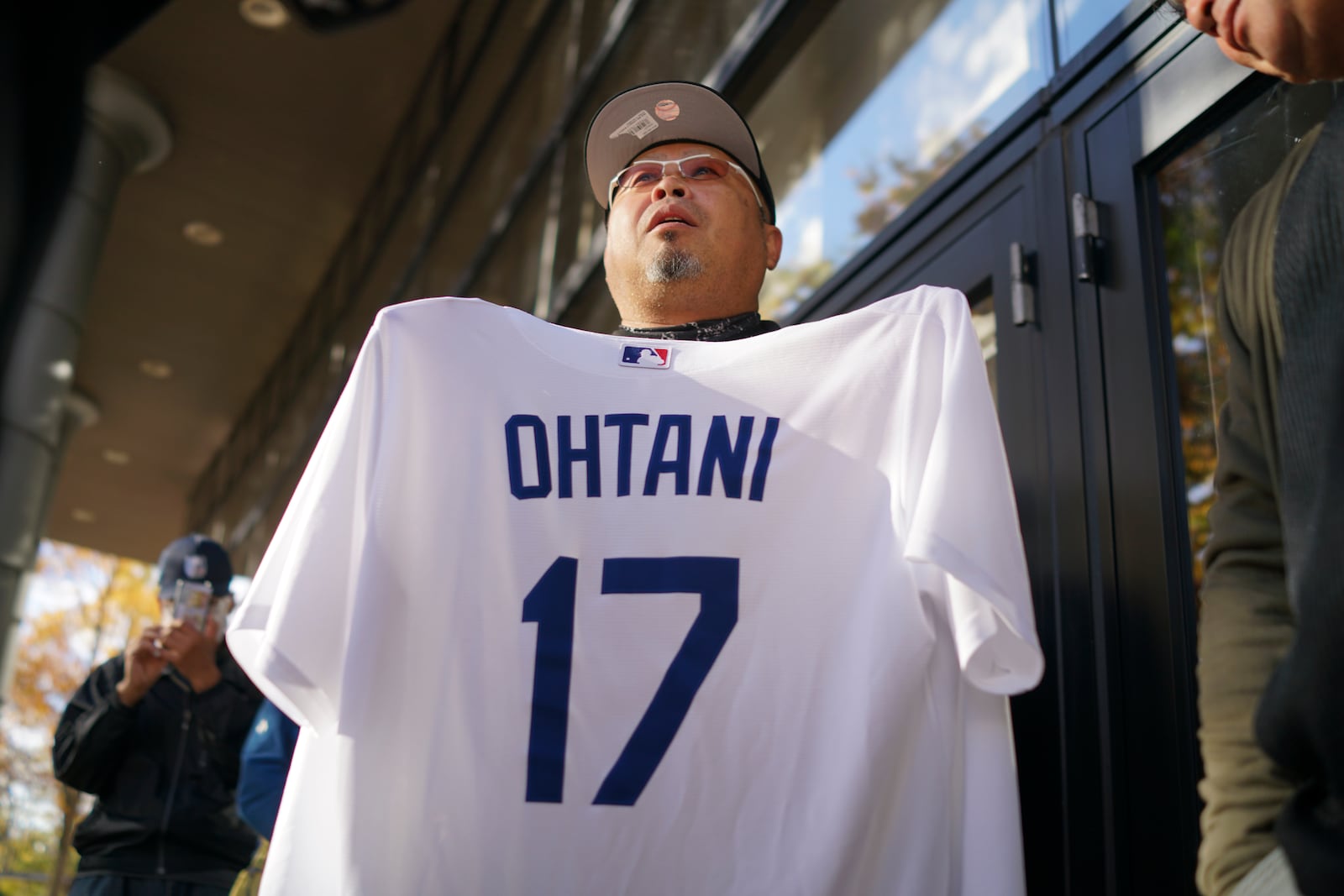 A man shows off a baseball jersey of Shohei Ohtani of the Los Angeles Dodgers as he and others wait in line to watch a live stream of Game 3 of the baseball World Series between the Dodgers and the New York Yankees, in a public viewing event in Oshu, northeastern Japan, the hometown of Ohtani, Tuesday, Oct. 29, 2024. (AP Photo/Eugene Hoshiko)