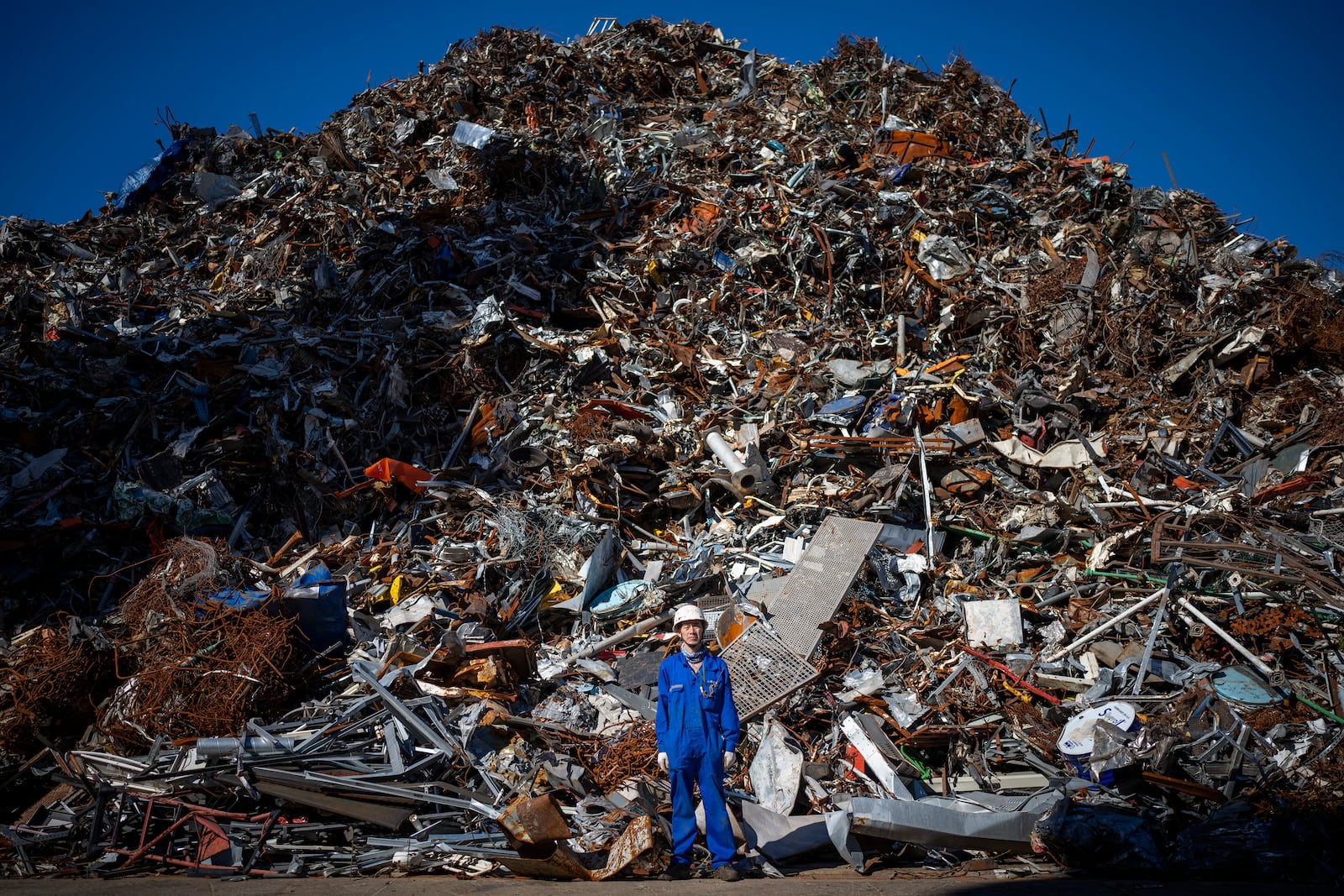 Ma Aijun, 45, of China, poses next to a mountain of scrap metal unloaded from the Chinese merchant ship he works on, at the port of Barcelona, Spain, Friday, Sept. 27, 2024. (AP Photo/Emilio Morenatti)