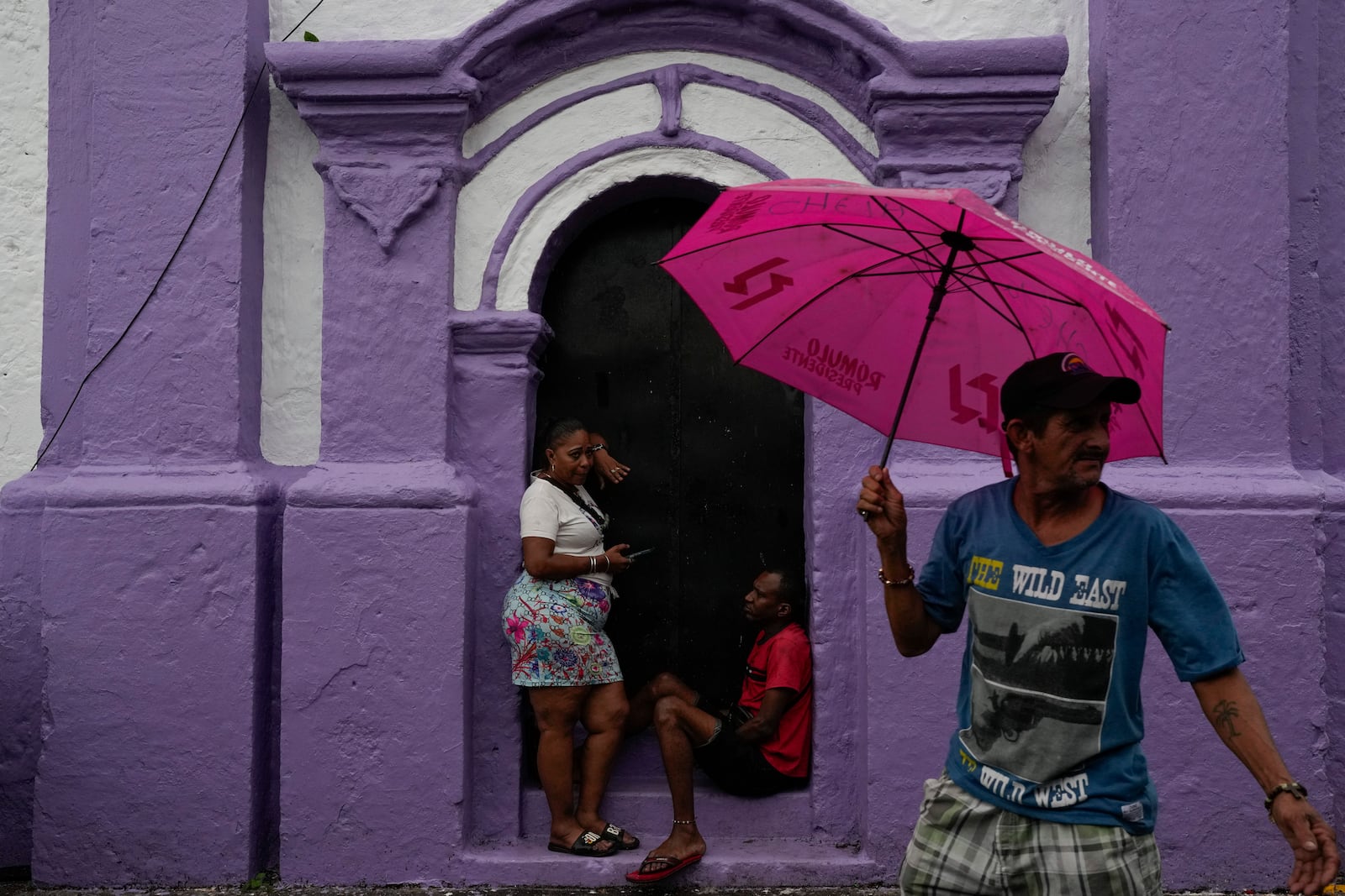 People take cover from rain at San Felipe Church in Portobelo, Panama, Sunday, Oct. 20, 2024, a day before the Black Christ festival. (AP Photo/Matias Delacroix)