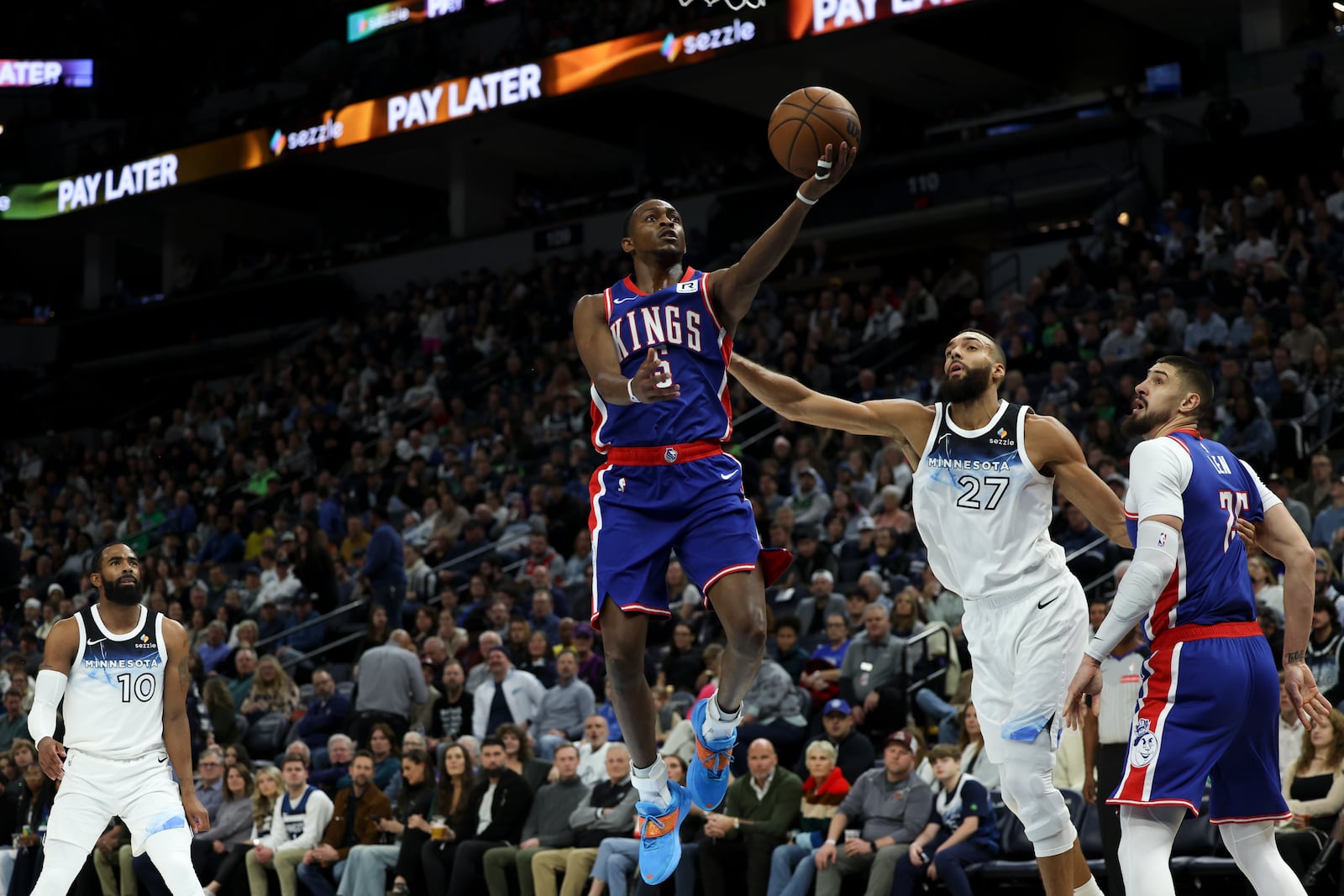 Sacramento Kings guard De'Aaron Fox (5) elevates to shoot against Minnesota Timberwolves center Rudy Gobert (27) while Kings center Alex Len, right, looks on during the first half of an NBA basketball game, Wednesday, Nov. 27, 2024, in Minneapolis. (AP Photo/Ellen Schmidt)