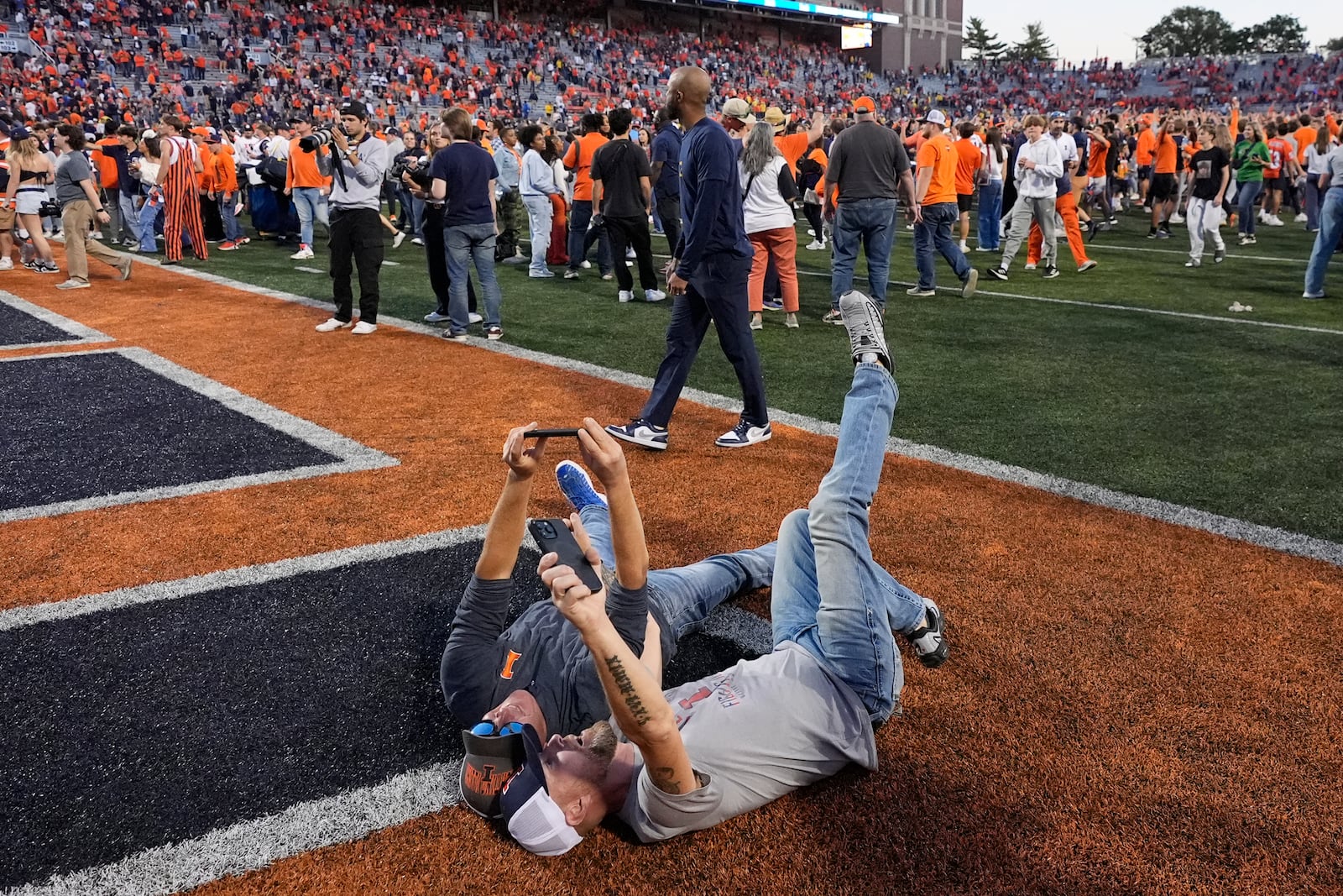 Two Illinois fans take selfies in the end zone after the team's 21-7 win over Michigan in an NCAA college football game Saturday, Oct. 19, 2024, in Champaign, Ill. (AP Photo/Charles Rex Arbogast)