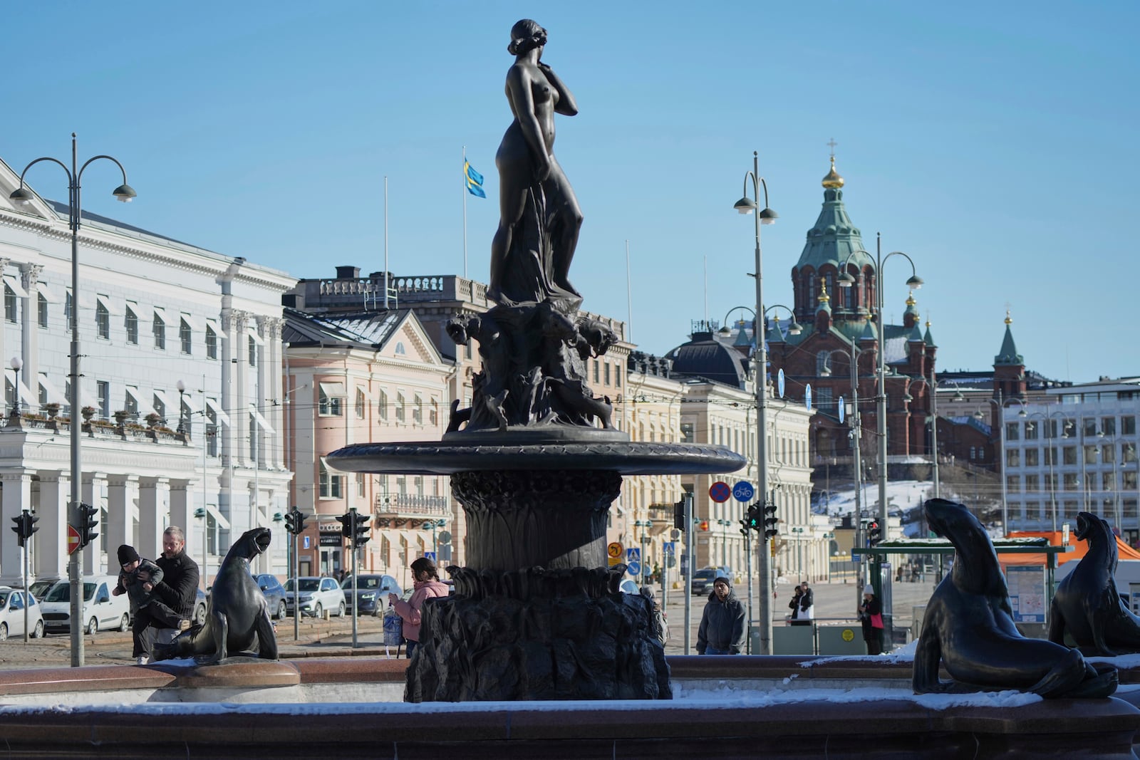 People walk next to the Havis Amanda statue on the Market Square in the center of Helsinki, Finland, Saturday, March 15, 2025. (AP Photo/Sergei Grits)