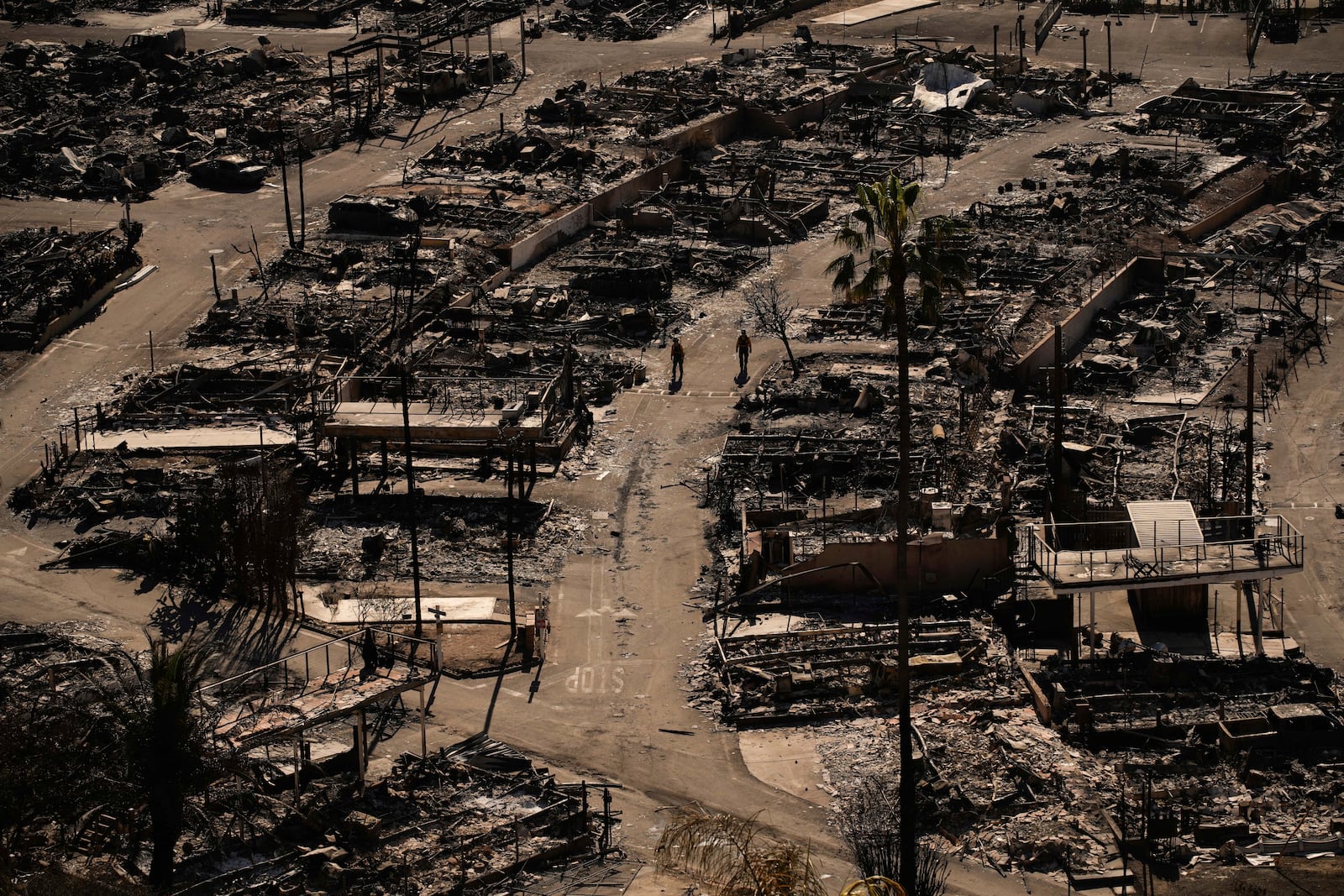 Two people walk along a road in a fire-ravaged community in the aftermath of the Palisades Fire in the Pacific Palisades neighborhood of Los Angeles, Monday, Jan. 13, 2025. (AP Photo/John Locher)