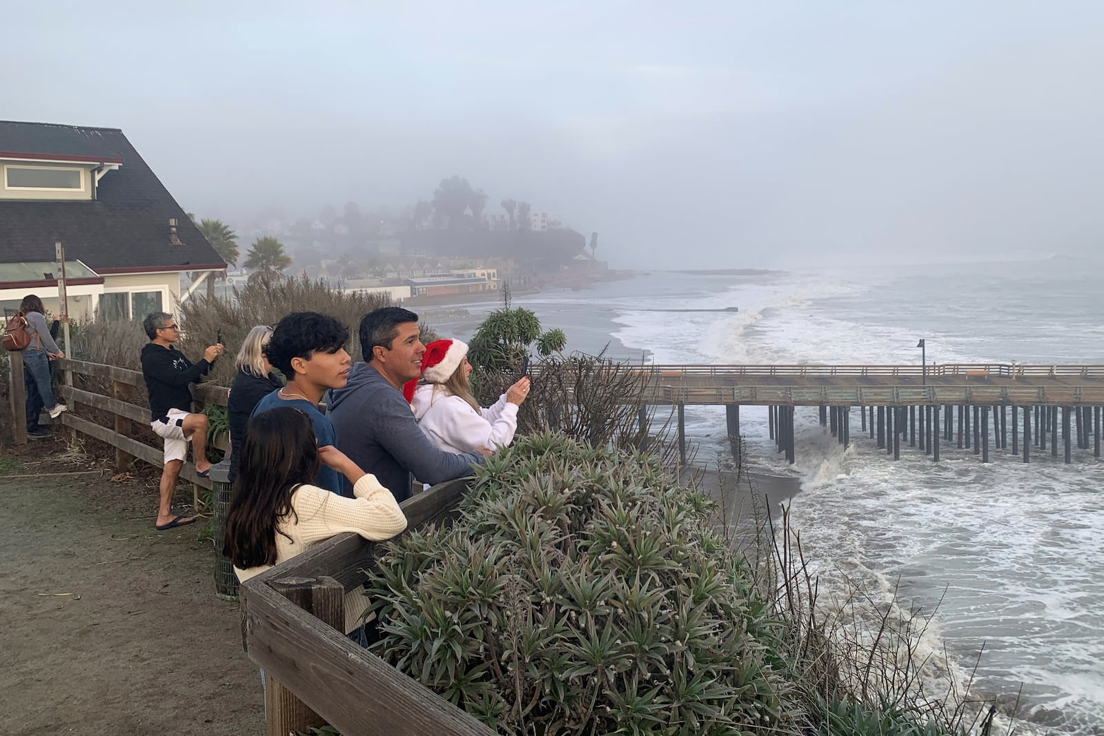 Spectators watch high surf roll in near the Capitola Wharf, Monday, Dec. 23, 2024, in Capitola, Calif. (AP Photo/Pamela Hassell)