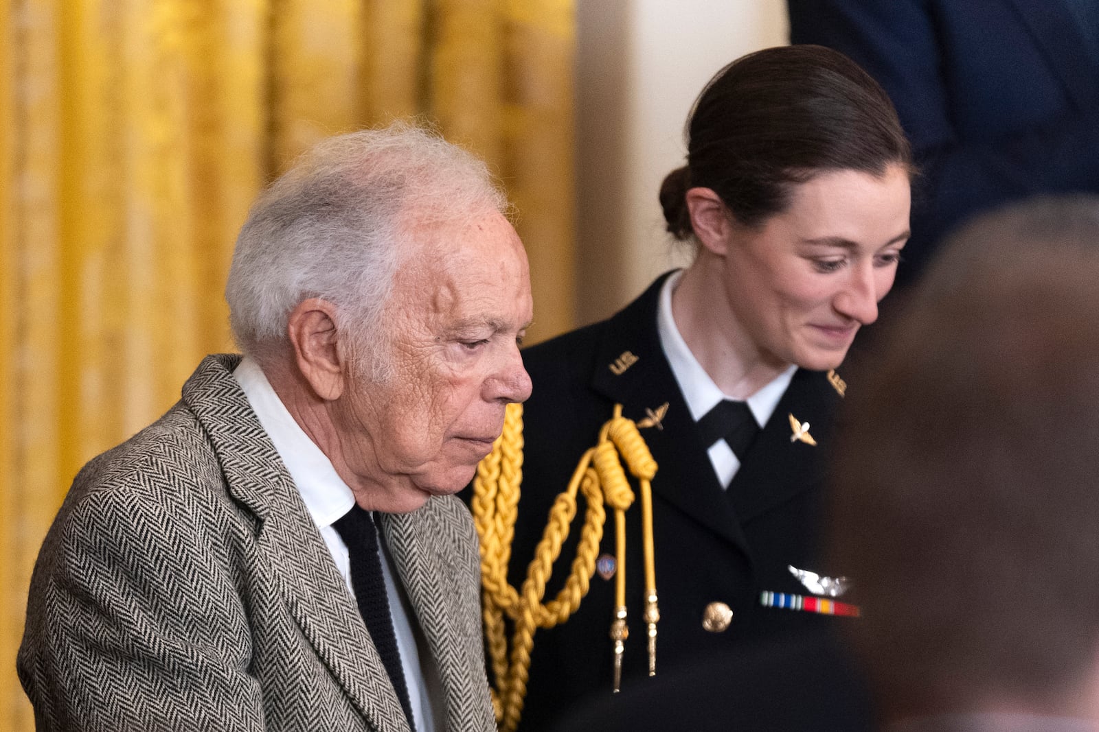 FILE - Army Capt. Rebecca M. Lobach, right, of Durham, N.C., escorts fashion designer Ralph Lauren during a ceremony honoring Lauren and 17 others with the Presidential Medal of Freedom in the East Room of the White House, Jan. 4, 2025, in Washington. (AP Photo/Manuel Balce Ceneta, File)