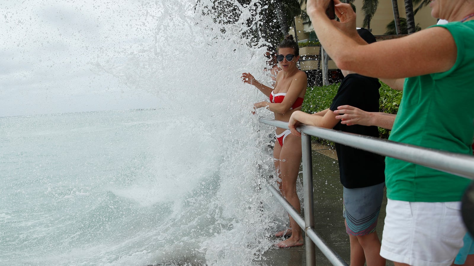 Elizabeth Dragan is splashed by a wave on a walkway along Waikiki Beach ahead of Hurricane Lane, Friday, Aug. 24, 2018, in Honolulu.