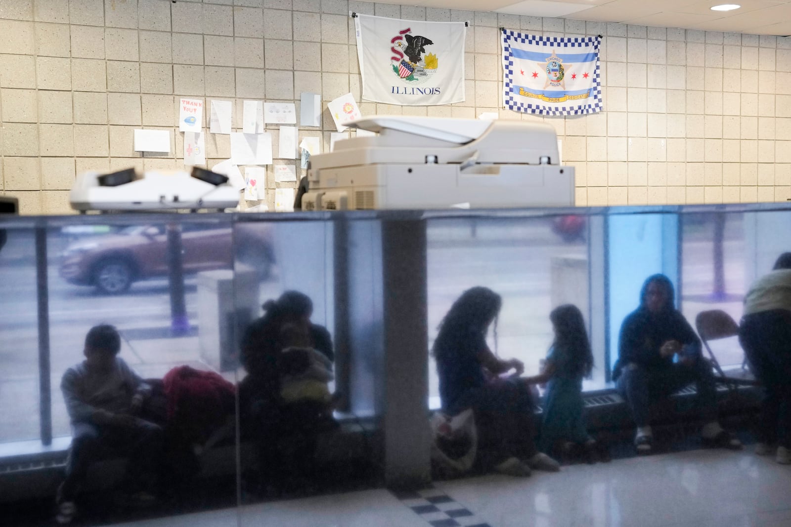 FILE - Immigrants from Venezuela are reflected in a marble wall while taking shelter at the Chicago Police Department's 16th District station on May 1, 2023. (AP Photo/Charles Rex Arbogast, FIle)