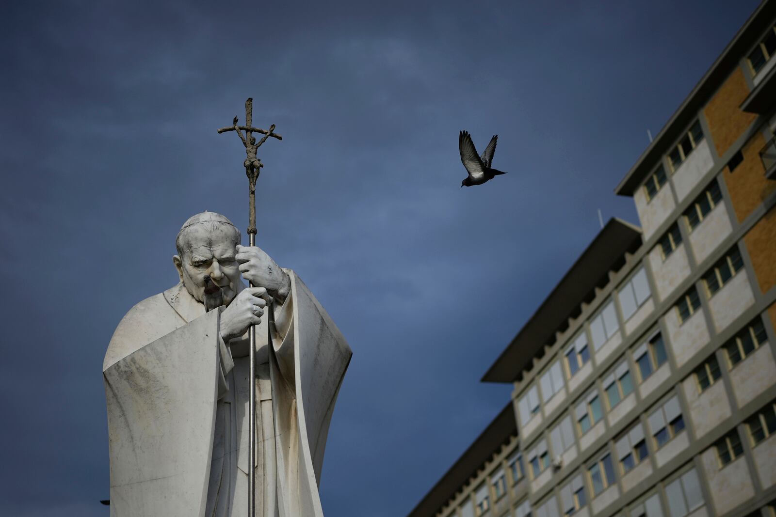 A marble statue of late Pope John Paul II is backdropped by the Agostino Gemelli Polyclinic in Rome, Saturday, Feb. 15, 2025, where Pope Francis was hospitalised Friday after a weeklong bout of bronchitis worsened and is receiving drug therapy for a respiratory tract infection. (AP Photo/Alessandra Tarantino)