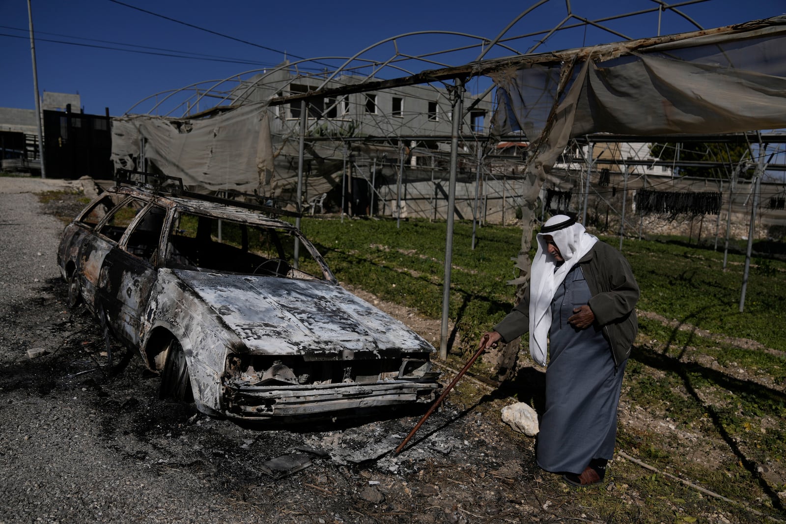 A Palestinian stands beside a torched car in the aftermath of an attack by Israeli settlers in the West Bank village of Jinsafut, Tuesday, Jan. 21, 2025. (AP Photo/Majdi Mohammed)