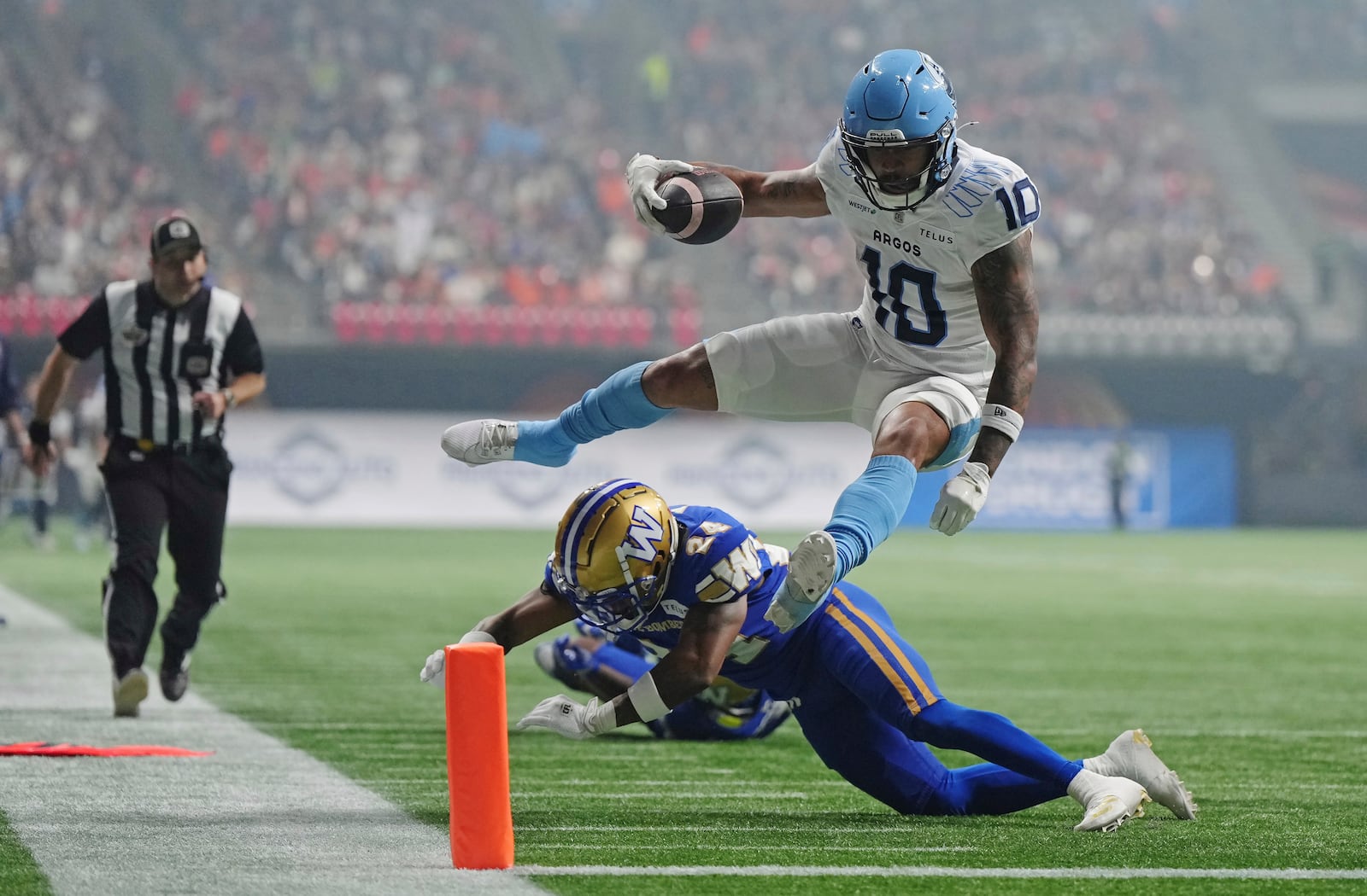 Toronto Argonauts' Kevin Mital (10) leaps to evade a hit from Winnipeg Blue Bombers' Terrell Bonds (24) and scores a touchdown during the second half of a CFL football game at the 111th Grey Cup in Vancouver, British Columbia, Sunday, Nov. 17, 2024. (Darryl Dyck/The Canadian Press via AP)