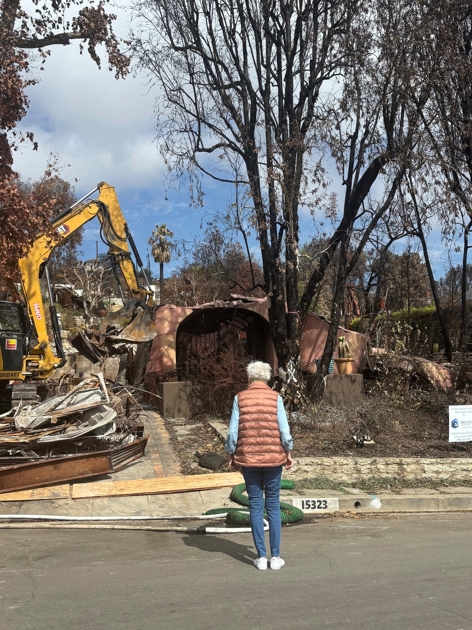 This image provided by Carolyn Kiefer shows her mother Katherine Kiefer, 82, looking at her burned home destroyed by the Palisades Fire where her cat Aggie went missing on Wednesday, Jan. 8, 2025, in Los Angeles. (Carolyn Kiefer via AP)