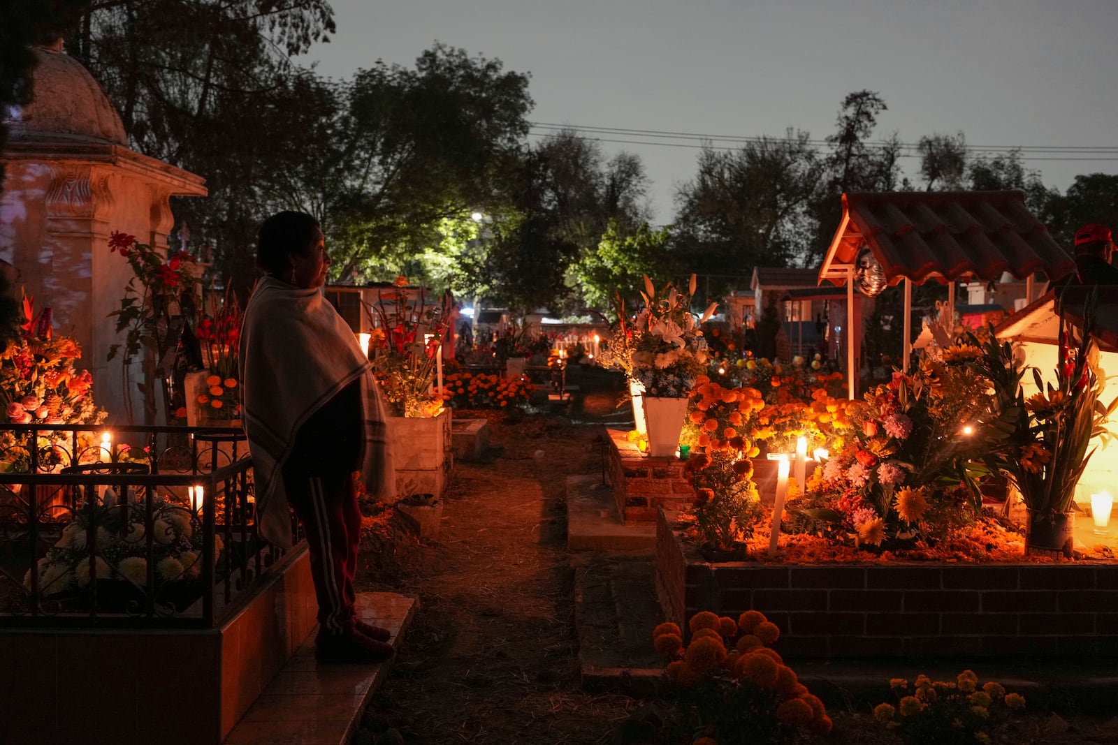 A woman stands at a tomb of a dearly departed, celebrating Day of the Dead, at the San Gregorio Atlapulco cemetery on the outskirts of Mexico City, Friday, Nov. 1, 2024. (AP Photo/Moises Castillo)