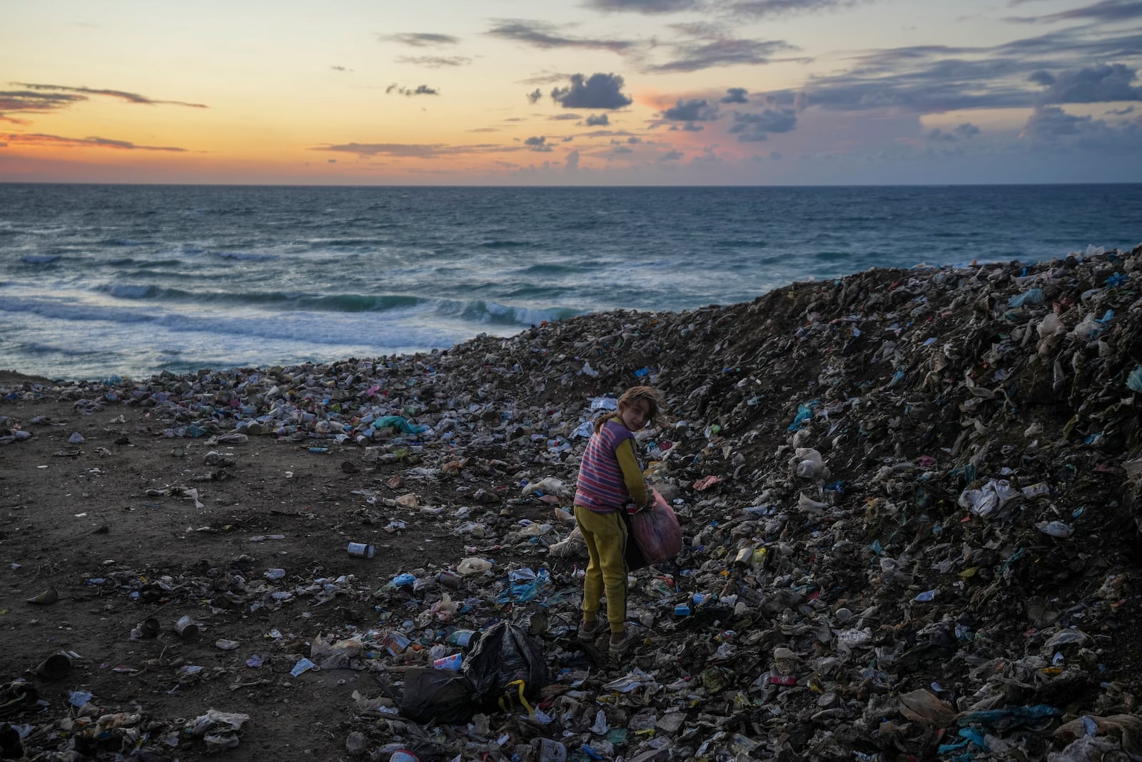 A girl tries to find something usable in the trash next to the tent camp for displaced Palestinians by the sea in Deir al-Balah, central Gaza Strip, Monday Dec. 30 2024.(AP Photo/Abdel Kareem Hana)